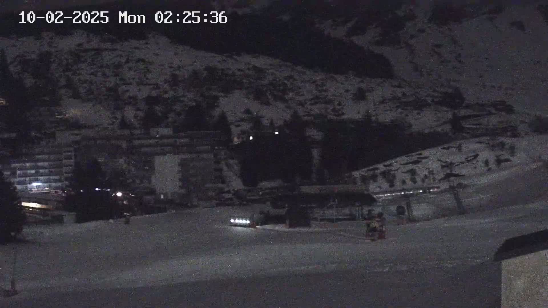 A snow-covered hillside at night is seen with several buildings and a few small lights visible near the bottom of the image.