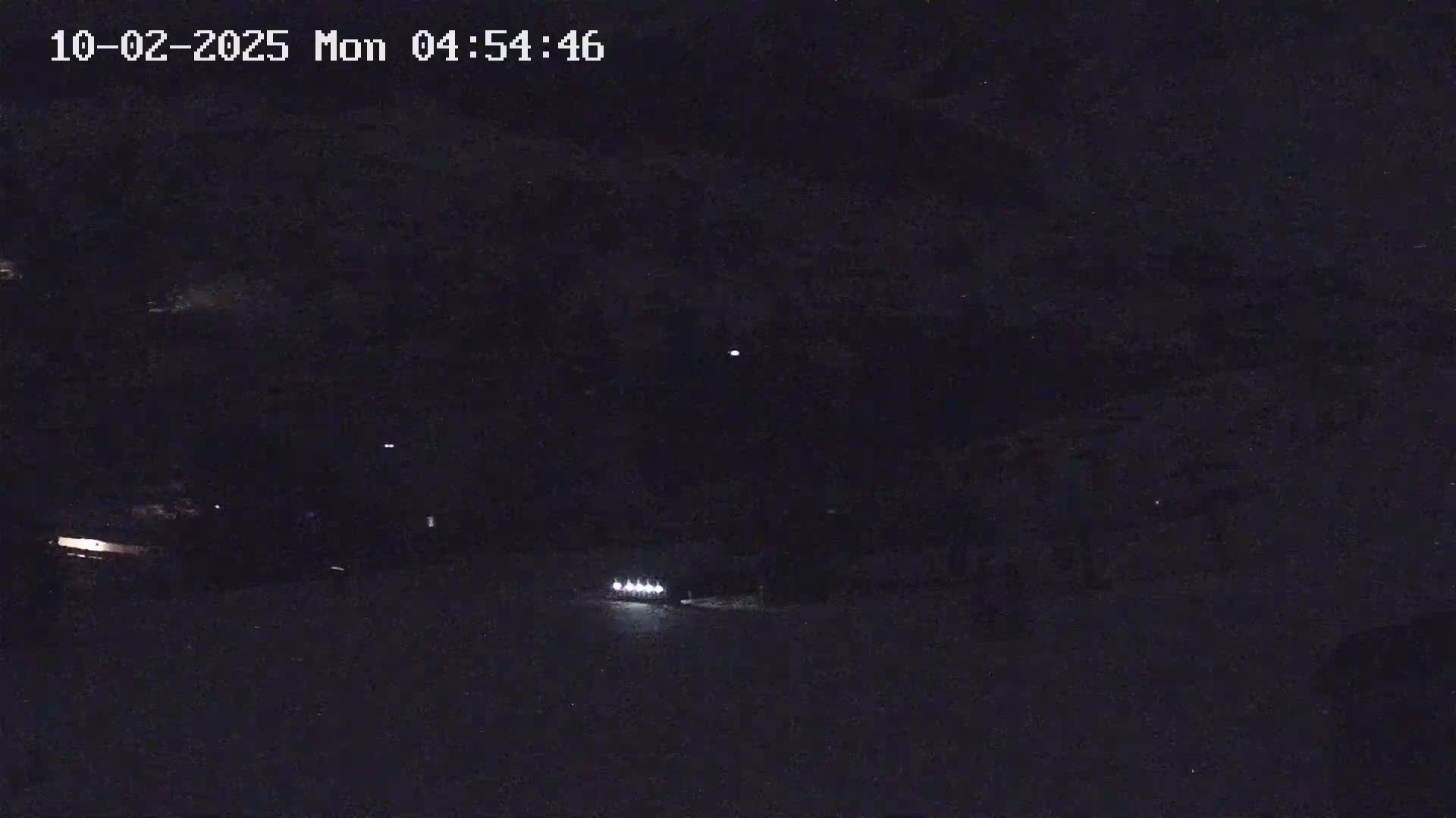A nighttime, low-light view shows a vehicle's headlights illuminating a dark, snowy or icy surface.