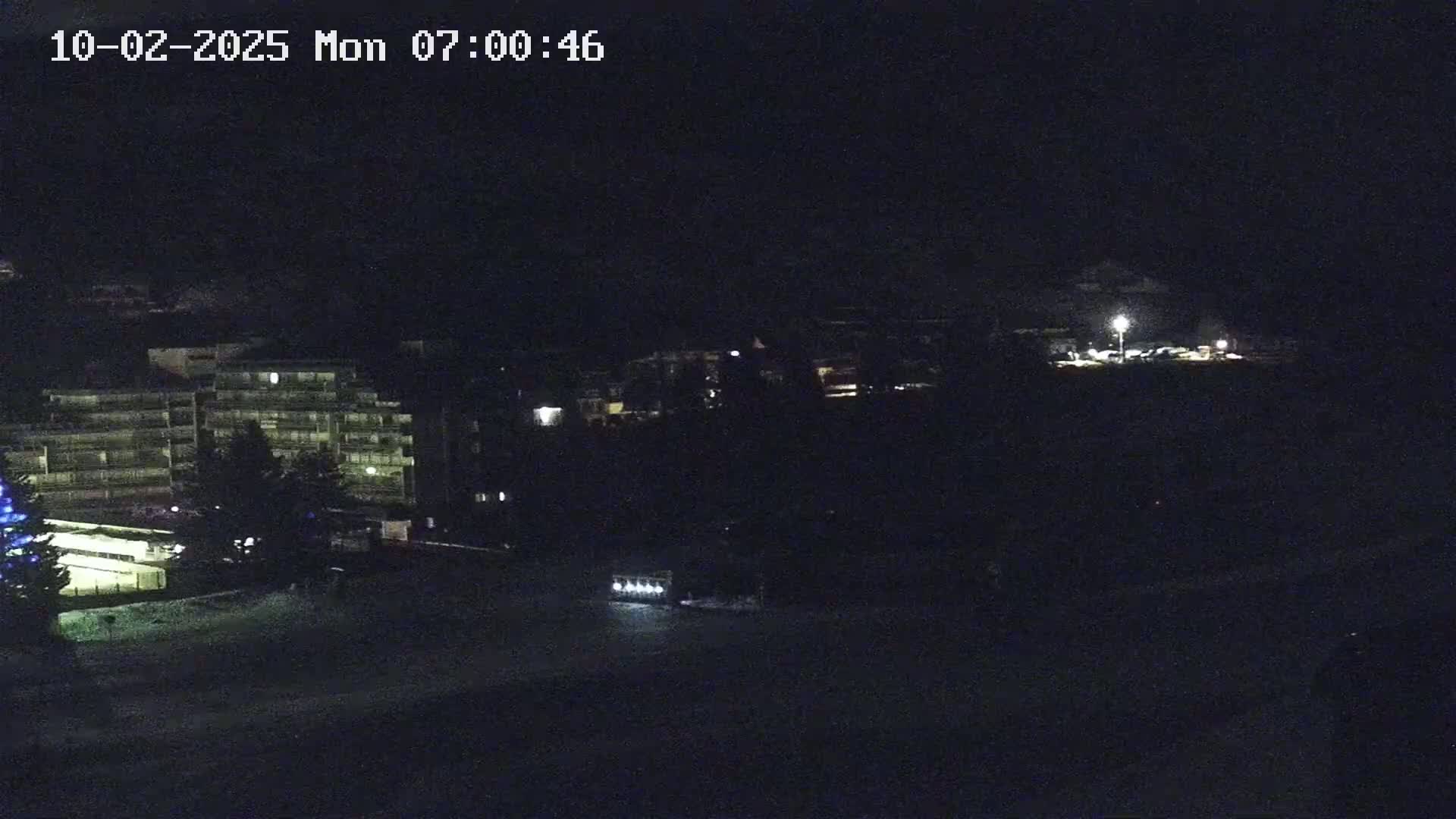 A nighttime view of a multi-story building and other structures, possibly in a snow-covered area.