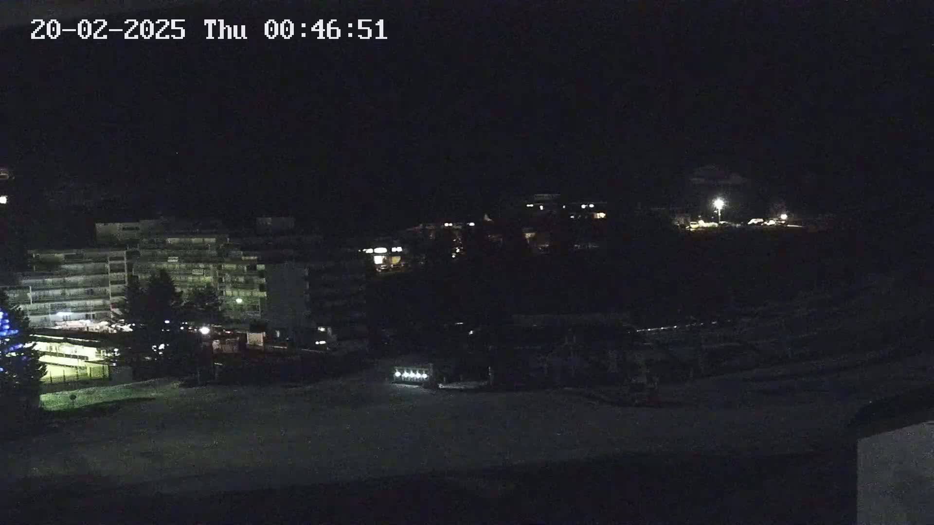 A nighttime view of several buildings illuminated by faint lights, with a snow-covered ground in the foreground.