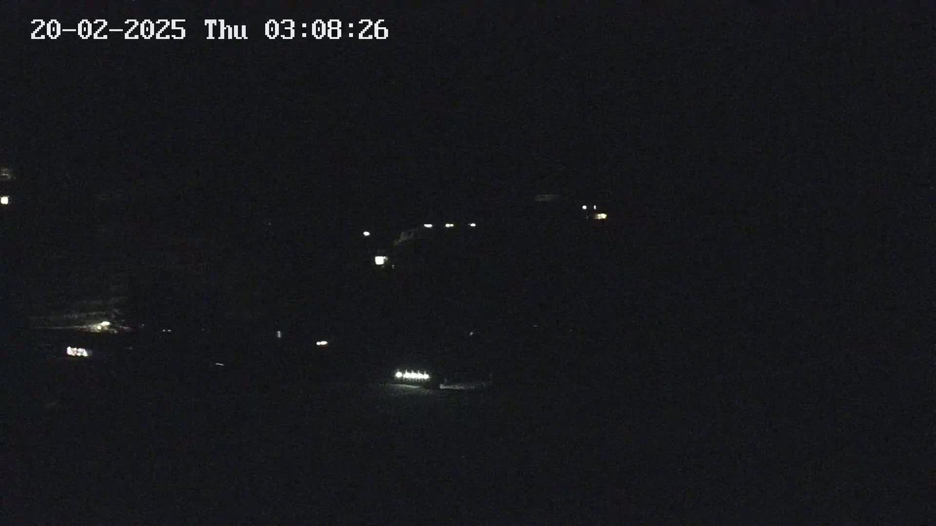 A nighttime, low-light view shows a dark road with a few distant lights from vehicles and buildings.