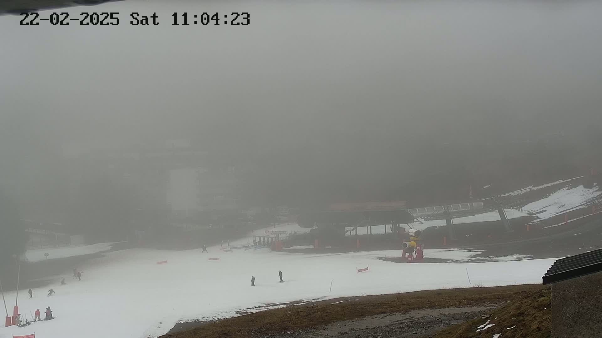 A foggy ski slope with a few skiers and a ski lift in the background.
