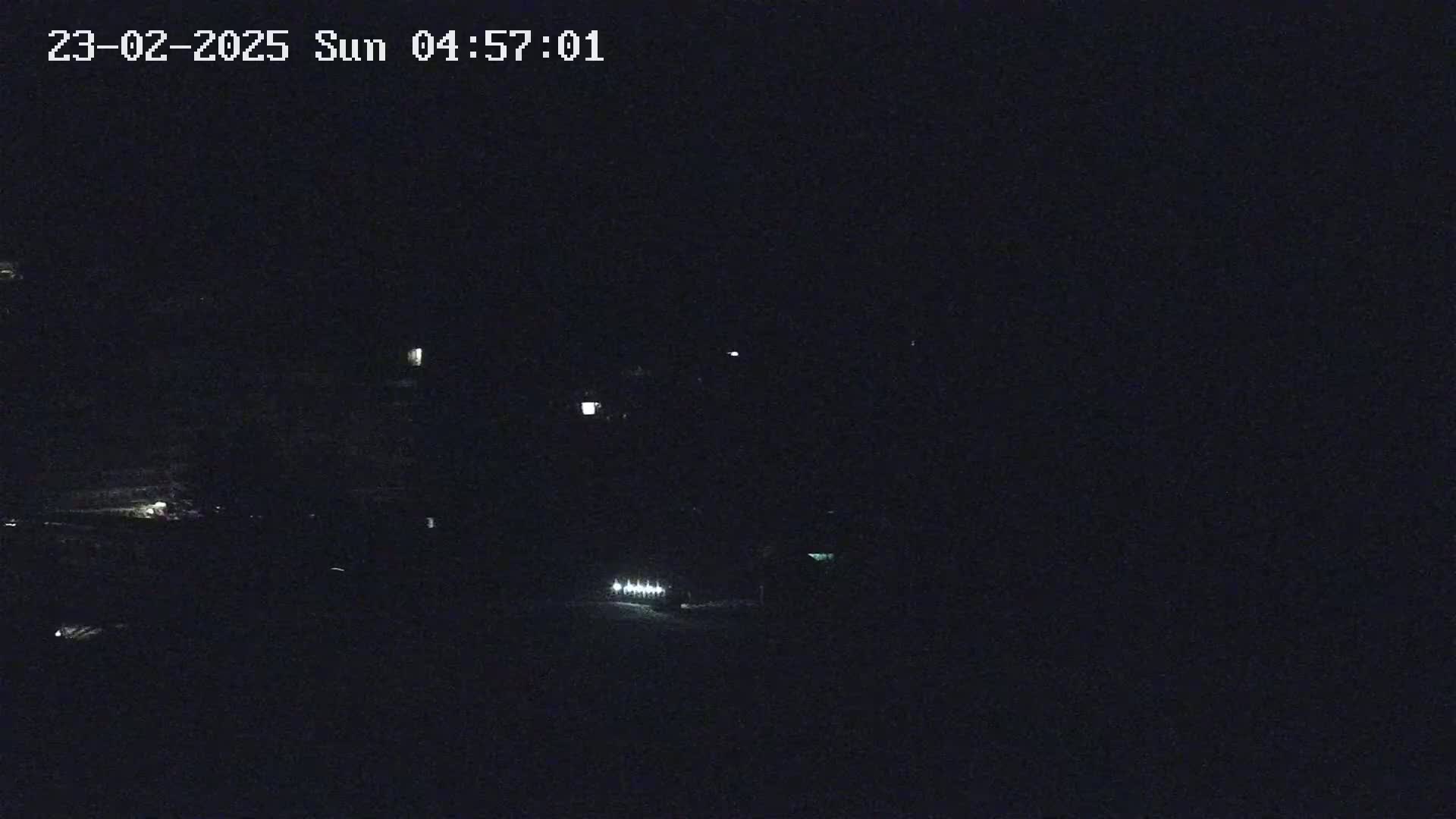 A nighttime, dark outdoor scene shows faint lights in the distance.