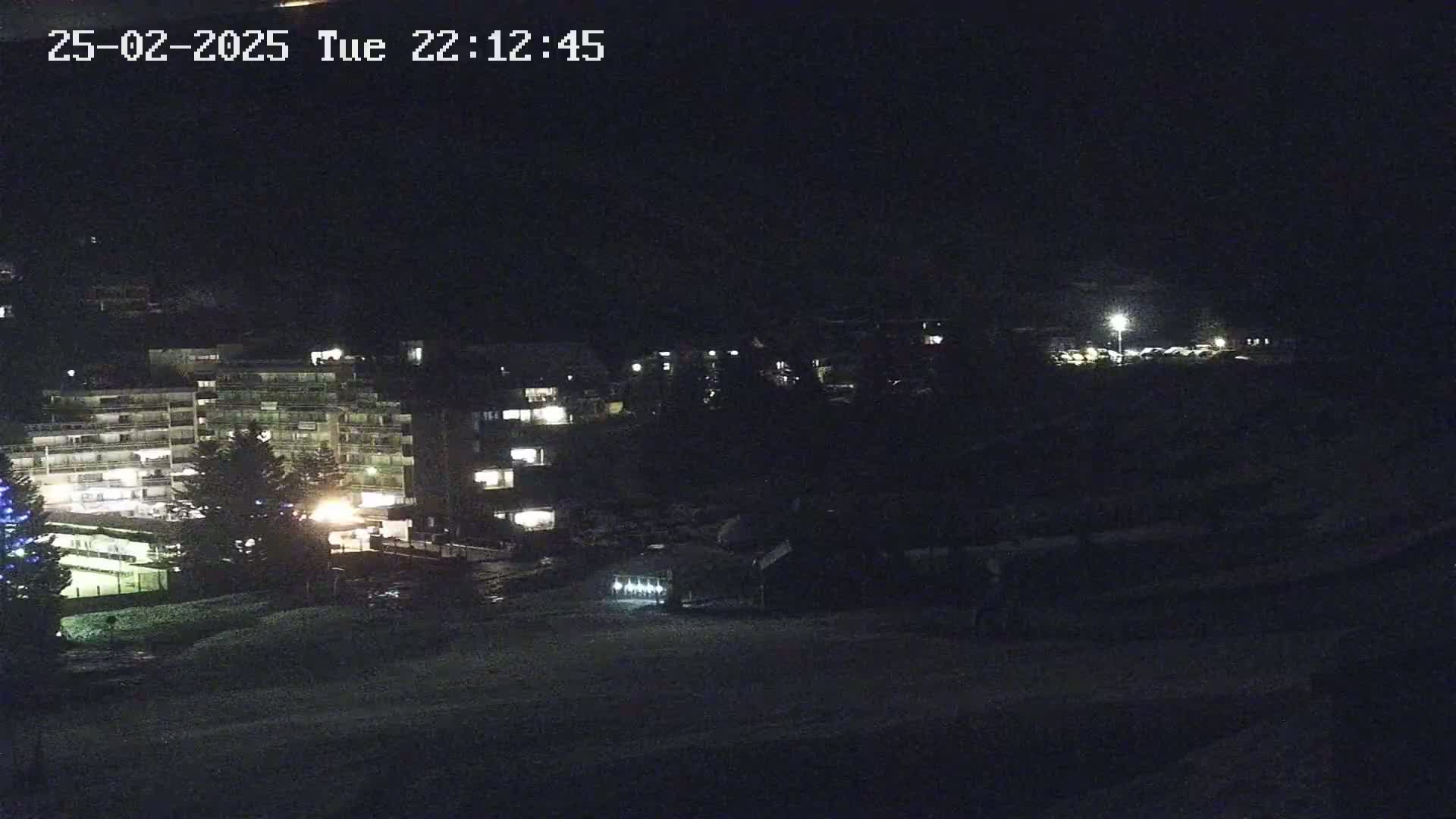 A nighttime view of snow-covered ground in front of several lit apartment buildings.