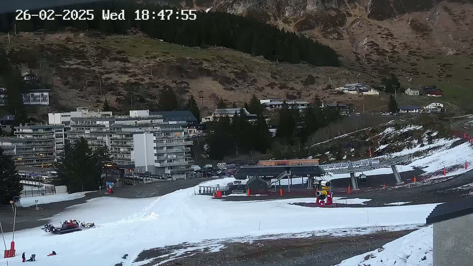 A snow-covered ski resort with a chairlift, a large apartment building, and several smaller buildings nestled into a mountainside at dusk.