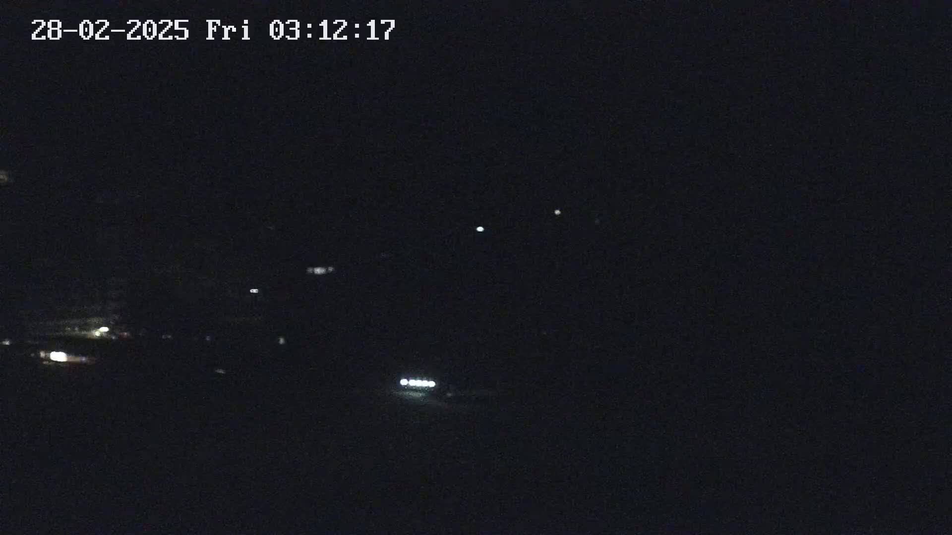 A nighttime, low-light image shows a few distant lights possibly from vehicles or buildings in the darkness.
