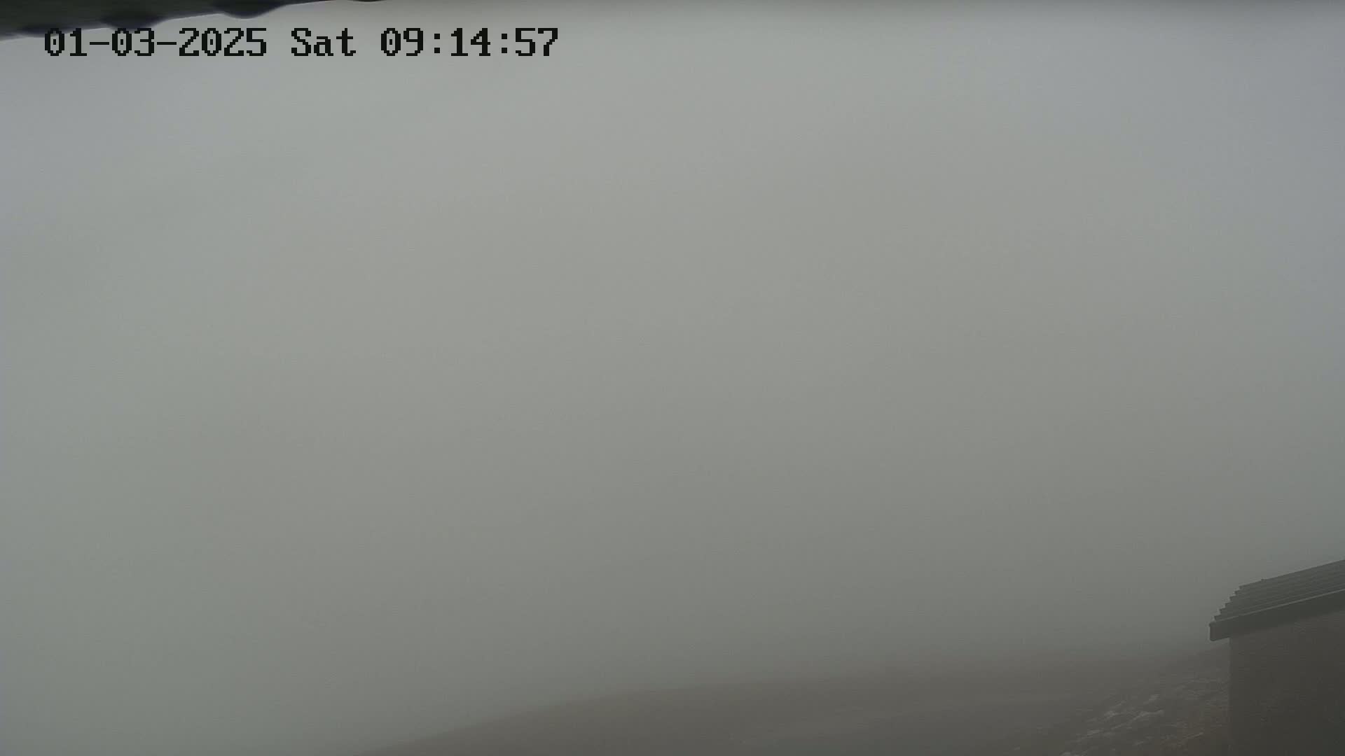 A thick fog obscures the view of a landscape, with only a portion of a roof visible in the bottom right corner.