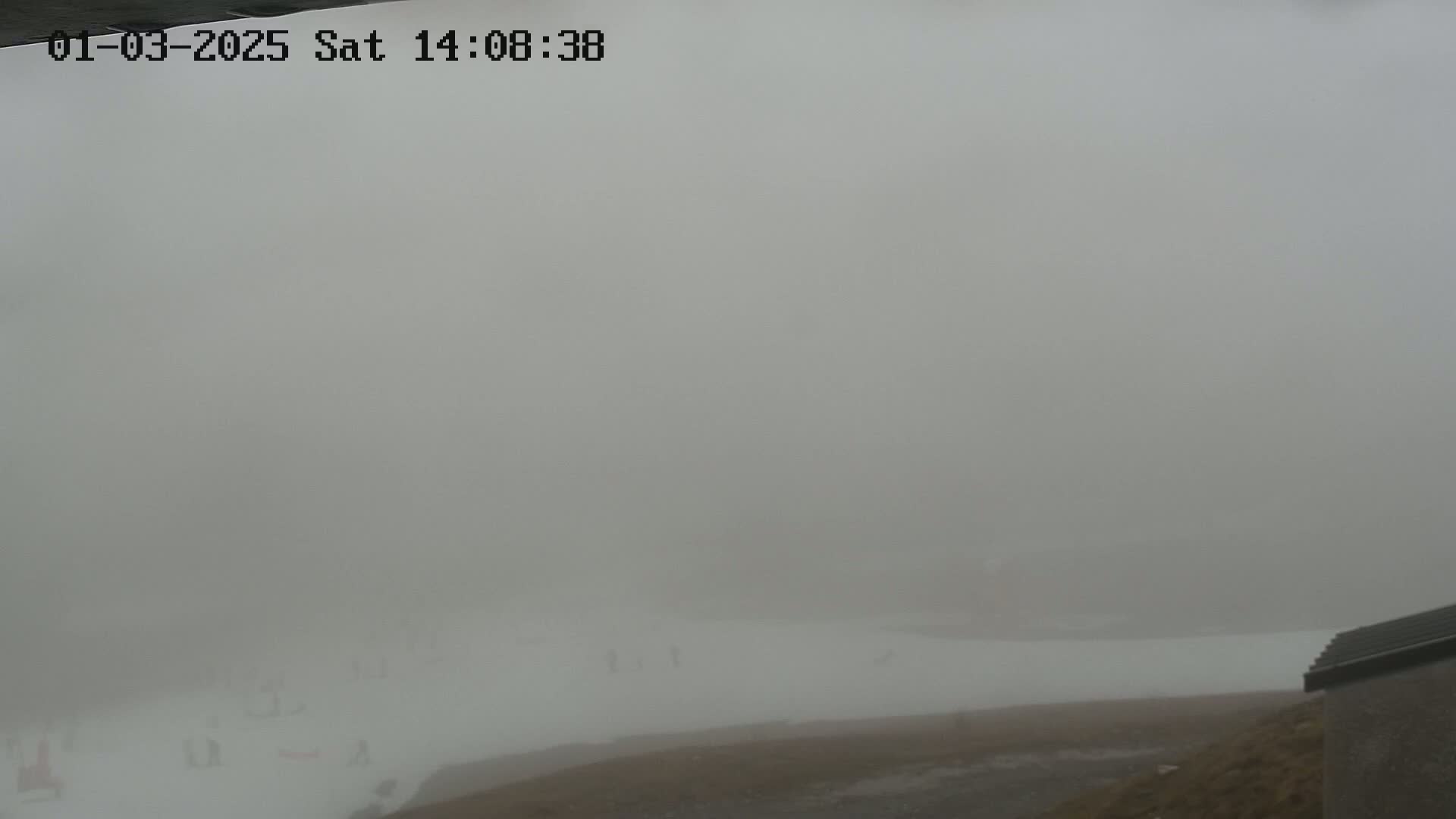 A foggy, outdoor scene shows a flat, snow-covered area with a glimpse of a building in the bottom right corner.