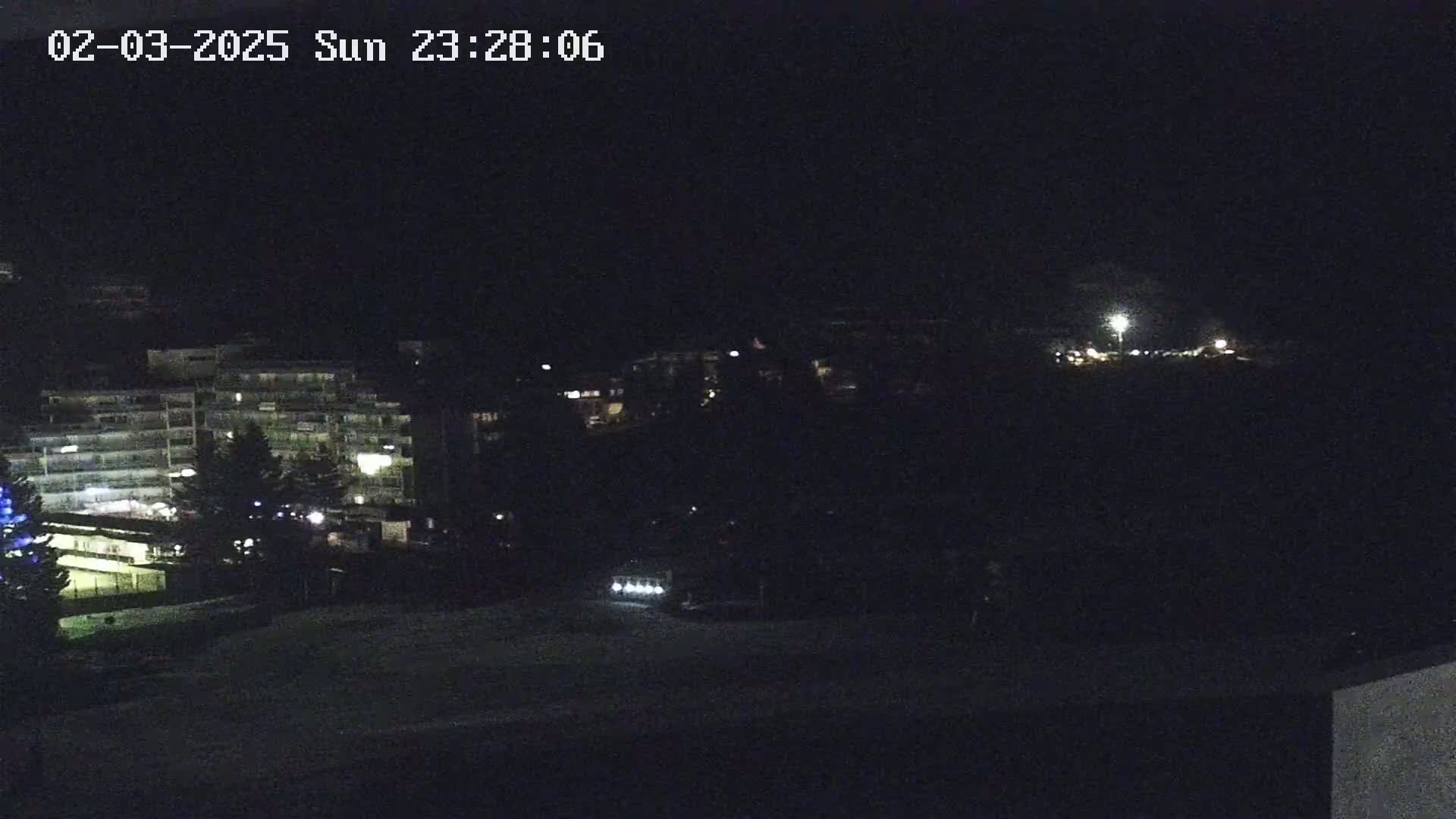 A nighttime view of a multi-story building and surrounding area, dimly lit with a few streetlights visible in the distance.