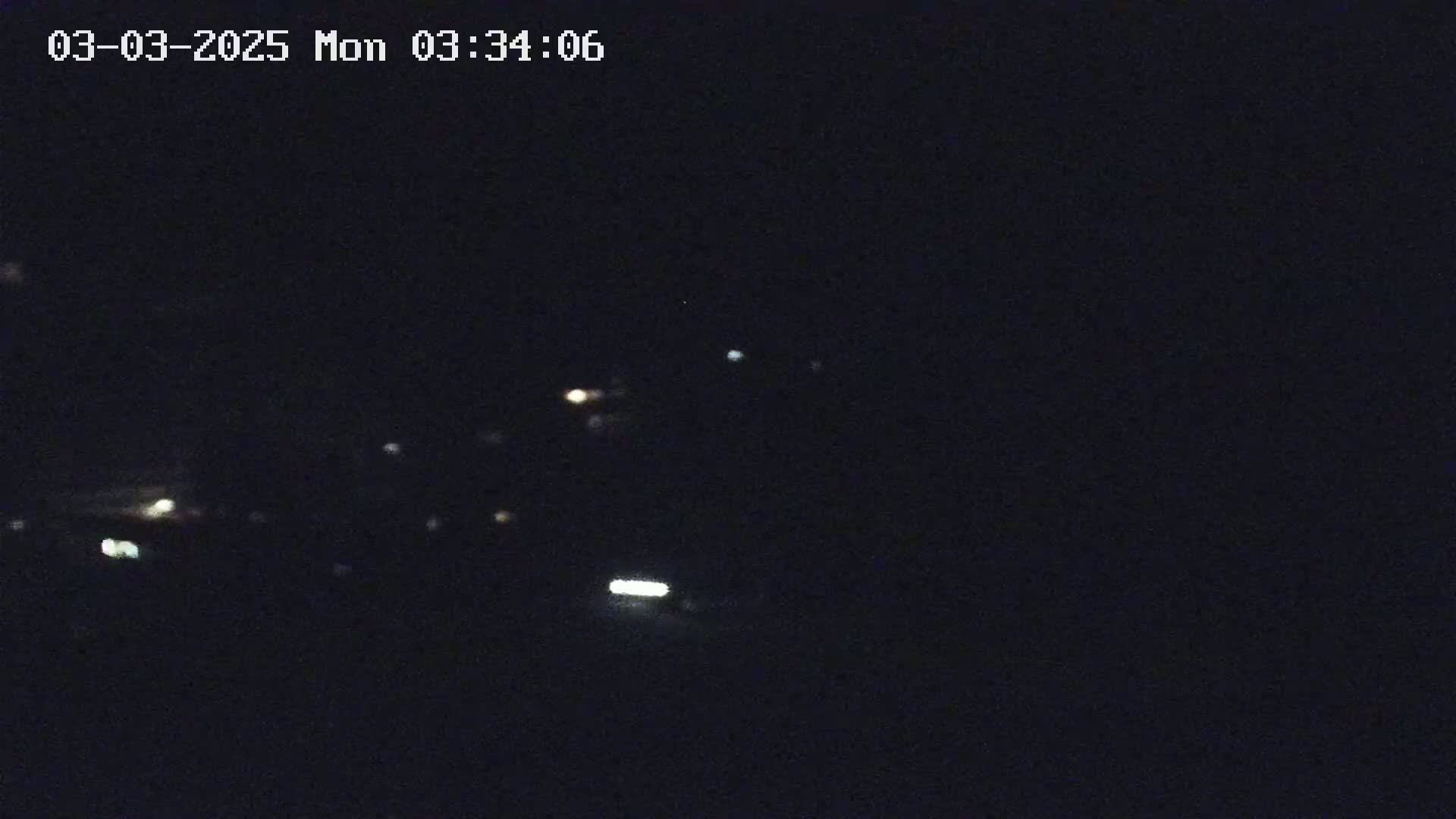 A nighttime long shot shows a few small lights scattered across a dark landscape.