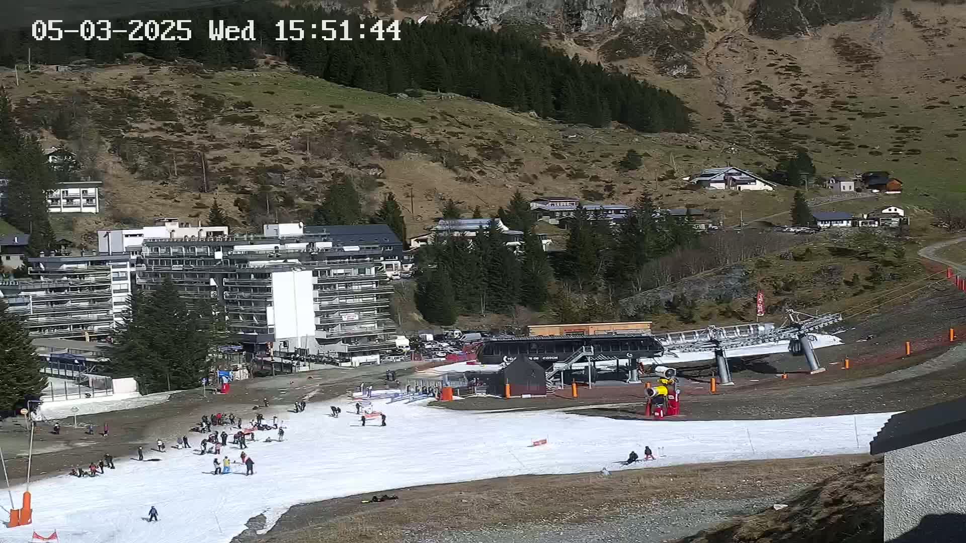 A ski slope with a chairlift and several buildings sits on a hillside under a sunny sky.
