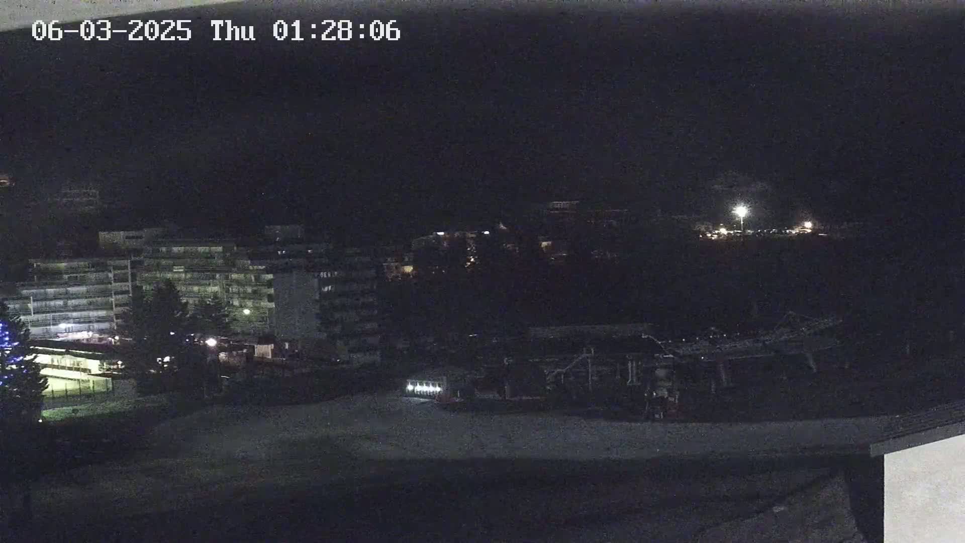 A nighttime view of a snow-covered area with buildings and some sparse lighting.
