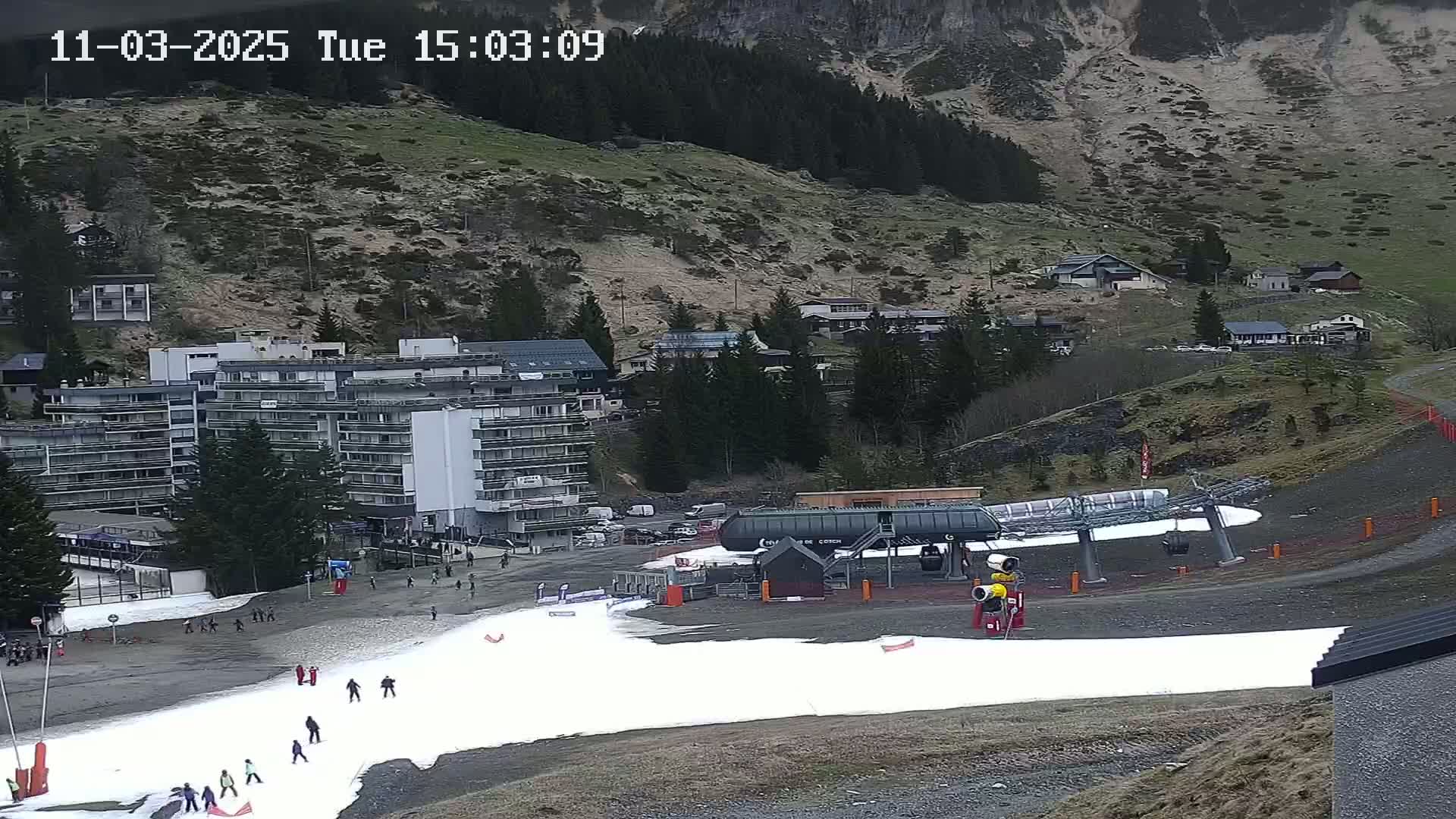 A ski resort with a chairlift and a small amount of snow on the ground, under an overcast sky.