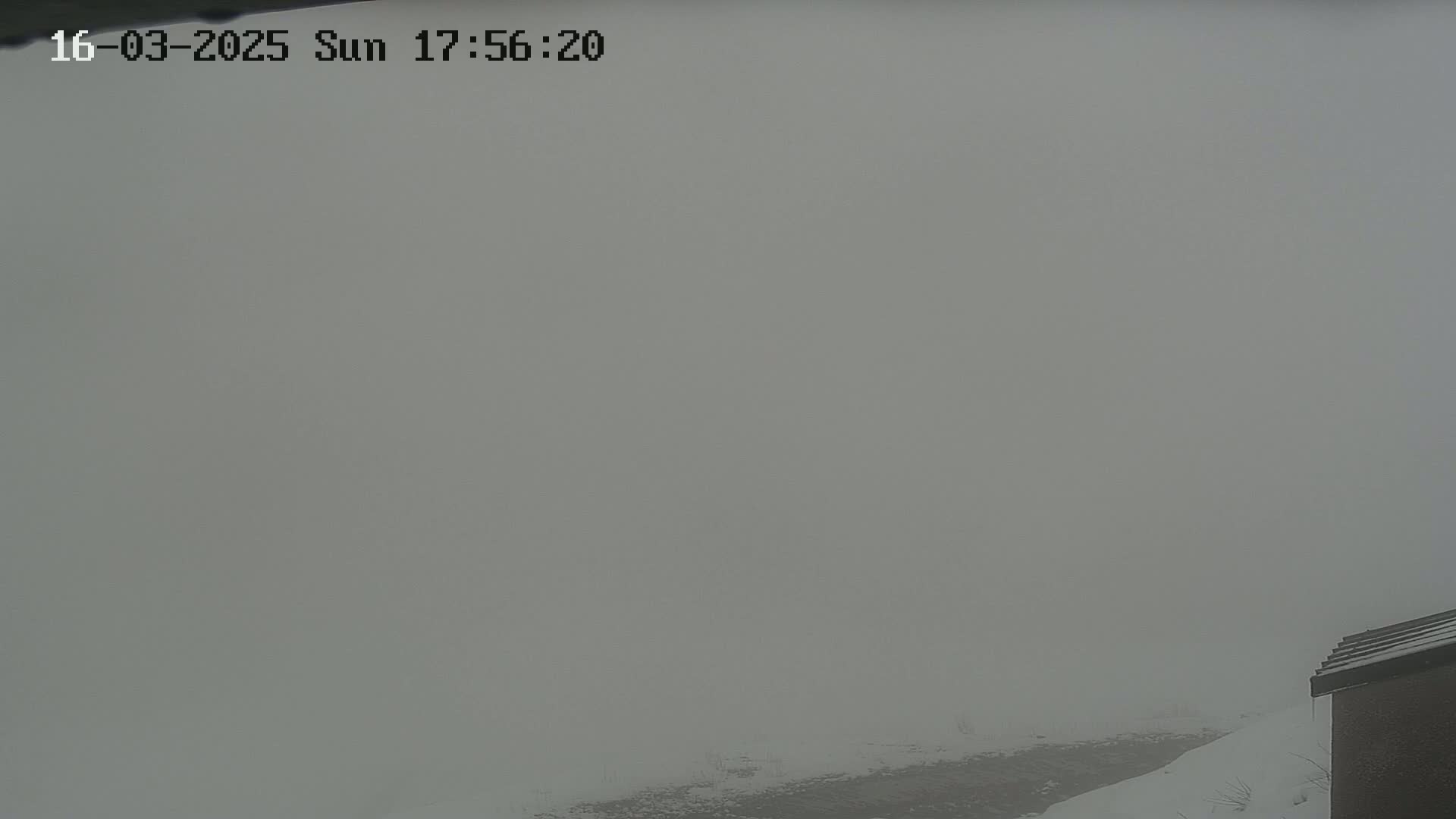 A foggy, snowy landscape is visible from a high vantage point, with a portion of a building's roof in the lower right corner.