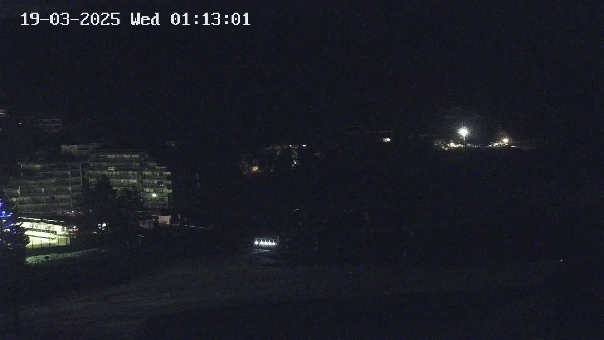 A nighttime, dimly lit view of a multi-story building and other structures, possibly in a residential area.
