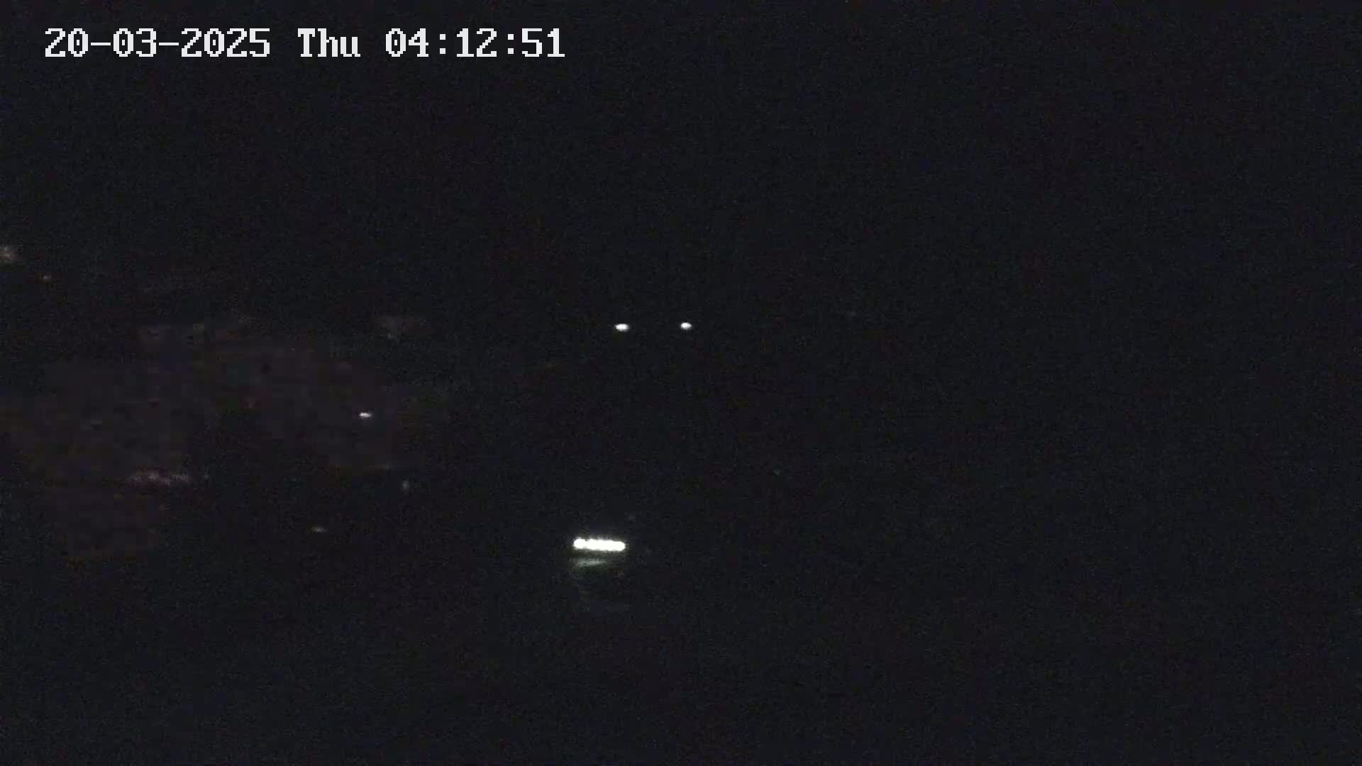 A nighttime, low-light outdoor scene shows a few faint lights in the distance.