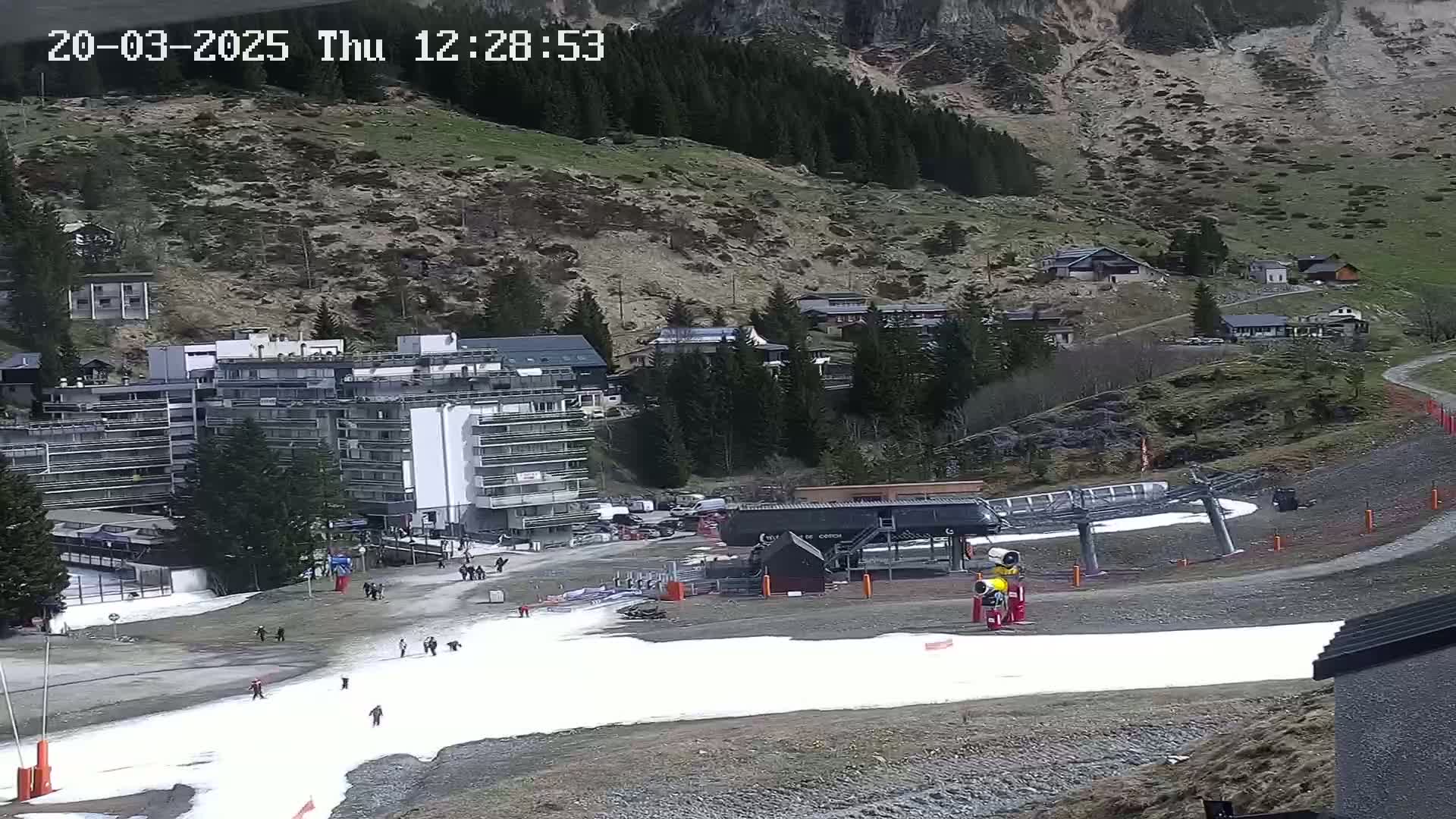 A ski resort with a large building, chairlift, and patches of snow on the ground, situated on a mountainside under a clear sky.