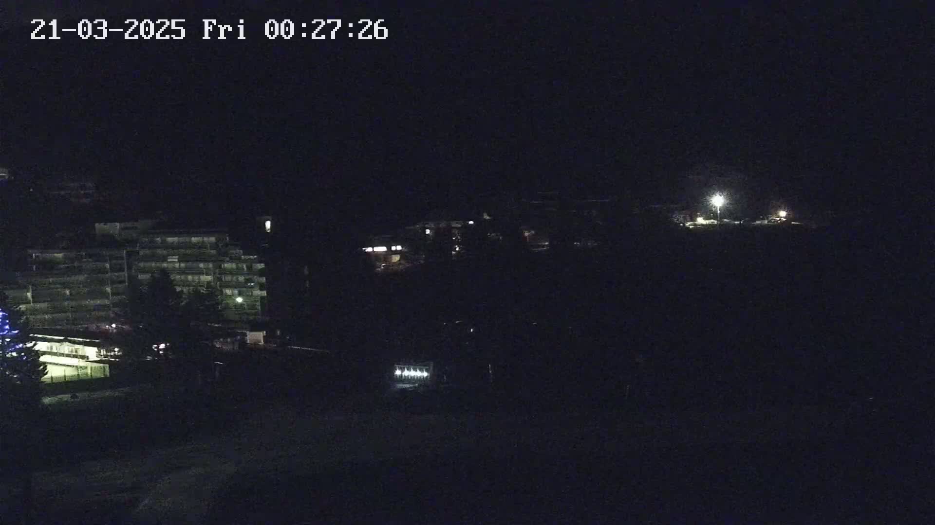 A nighttime long shot shows a dark landscape with dimly lit buildings and a few streetlights.