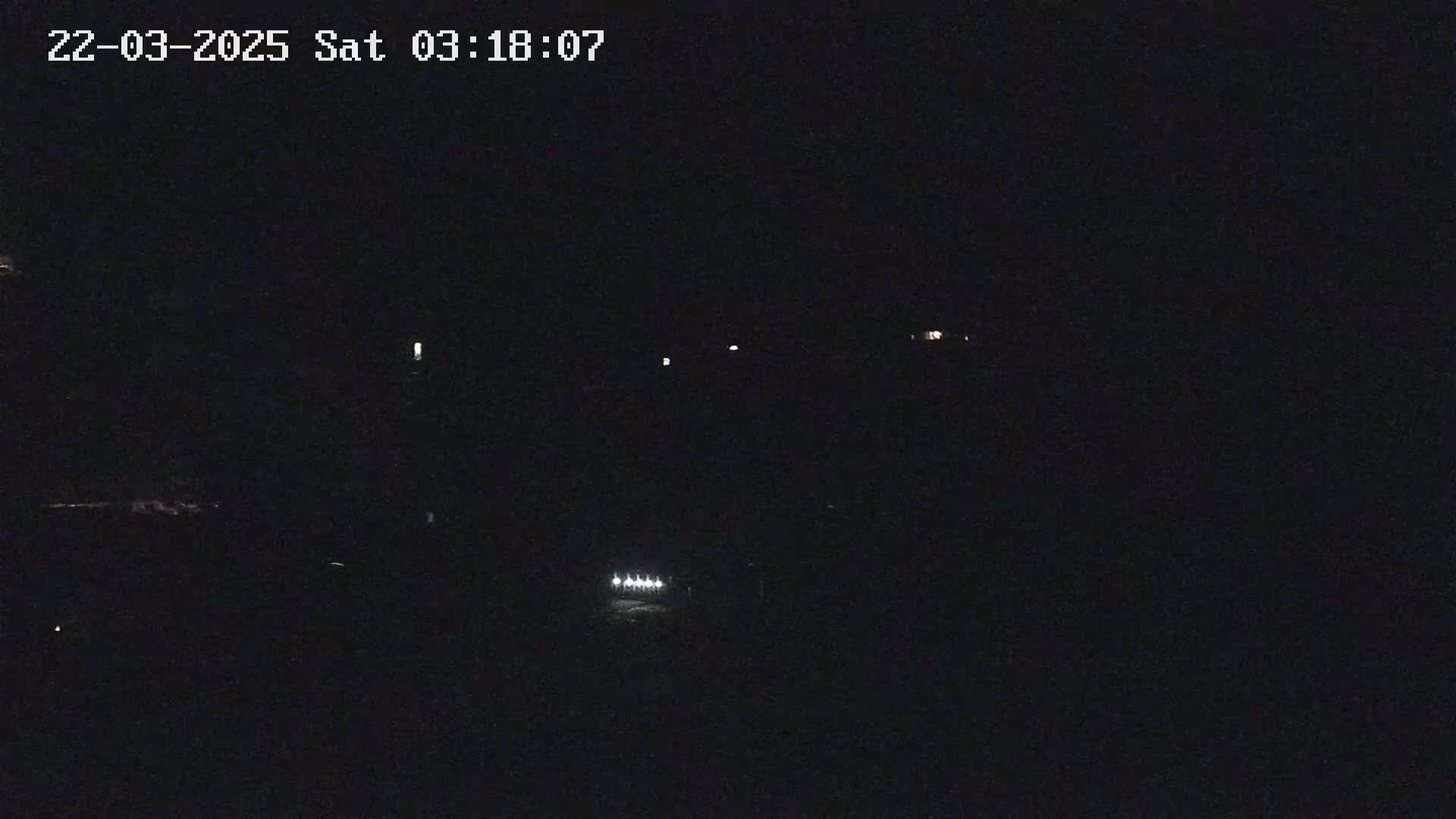 A nighttime, dark scene shows a few faint lights in the distance, possibly from vehicles or buildings.