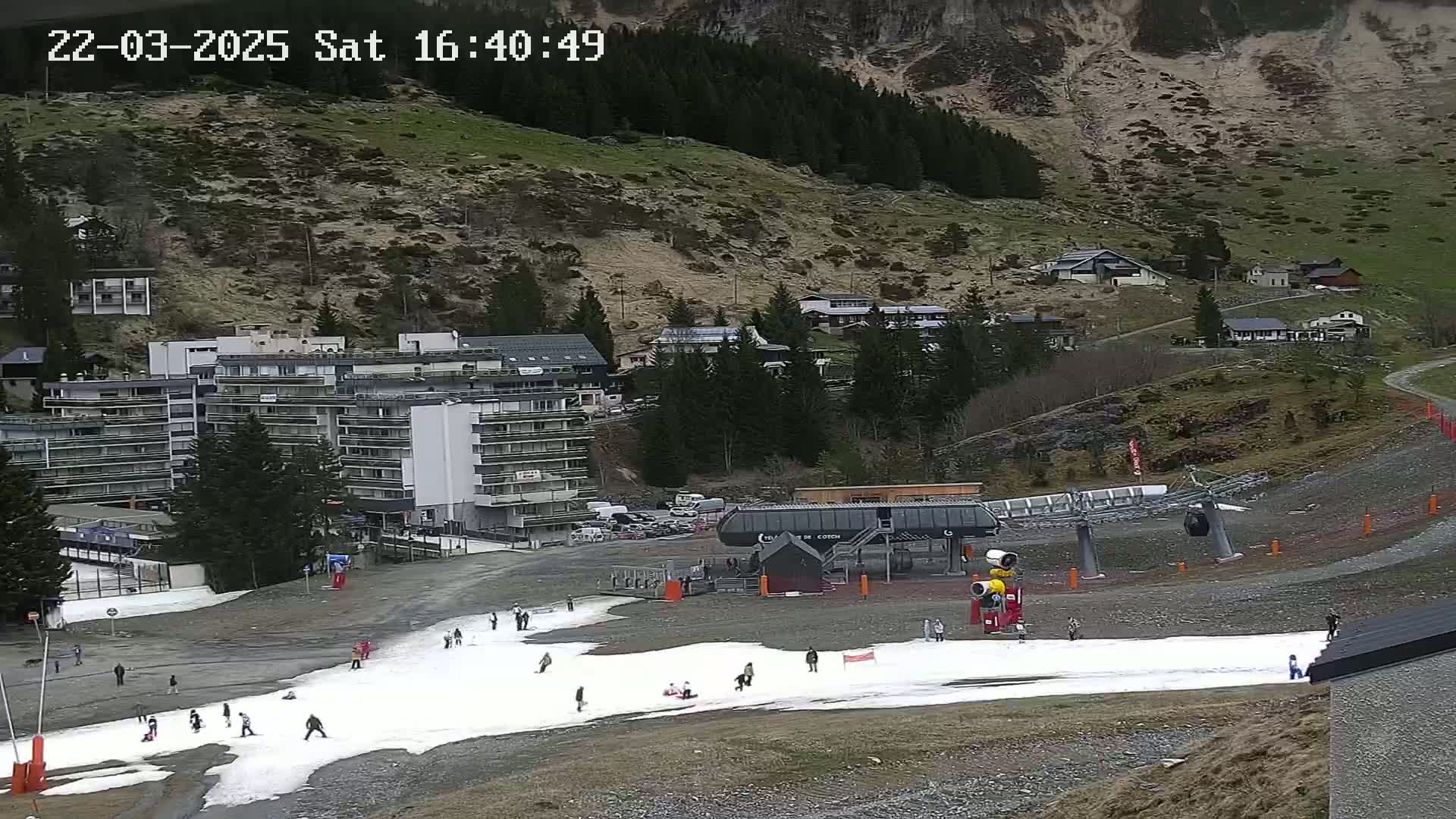 A ski lift and a small amount of snow are visible in a mountainside resort town under overcast skies.