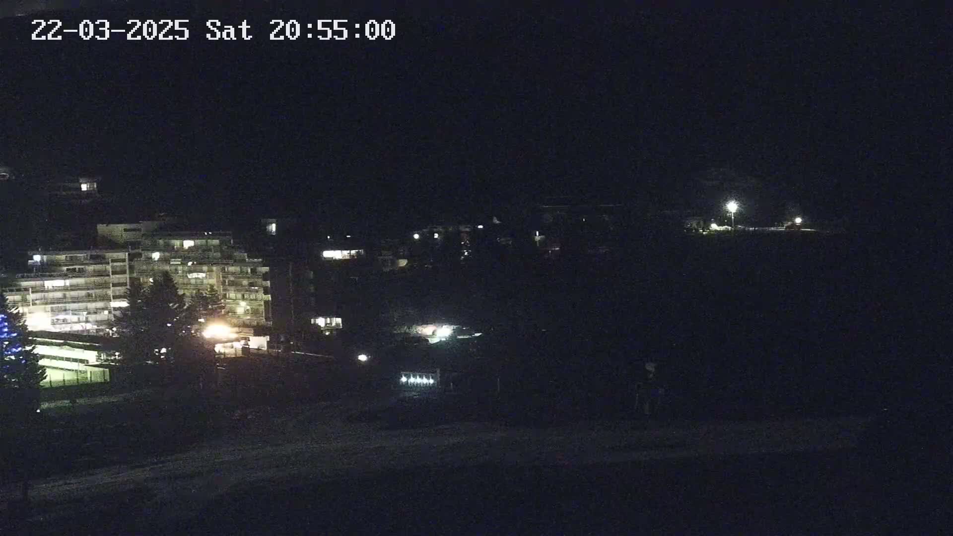 A nighttime view of a multi-story building complex, partially illuminated, with a few lights visible in the surrounding area.