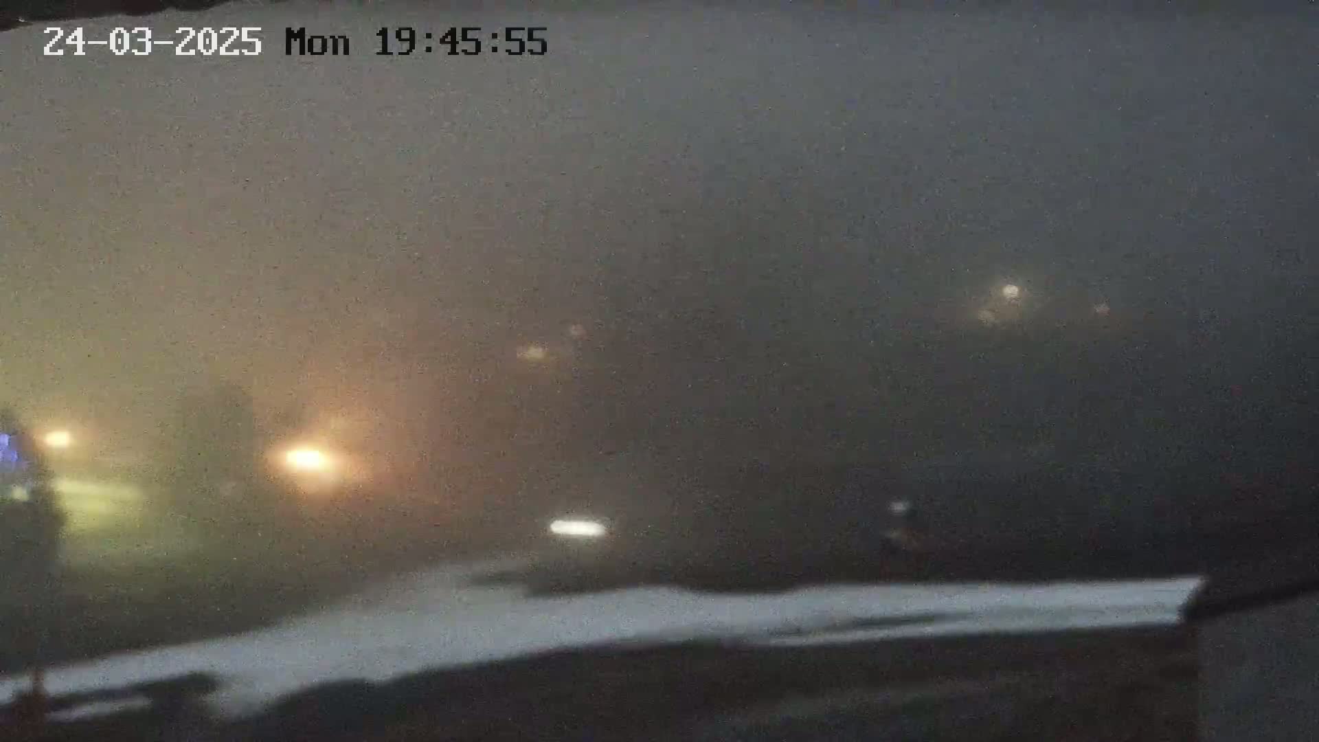 Headlights of vehicles are barely visible through a thick fog at night.