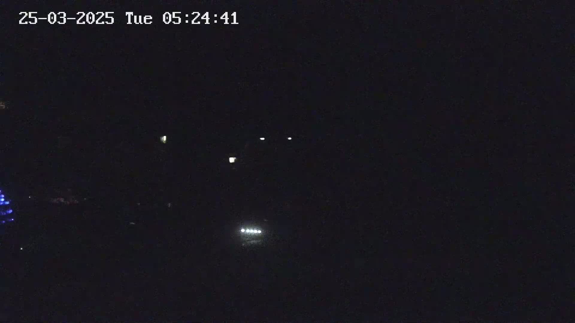 A nighttime, dark scene shows a few faint lights in the distance, possibly from vehicles or streetlights.