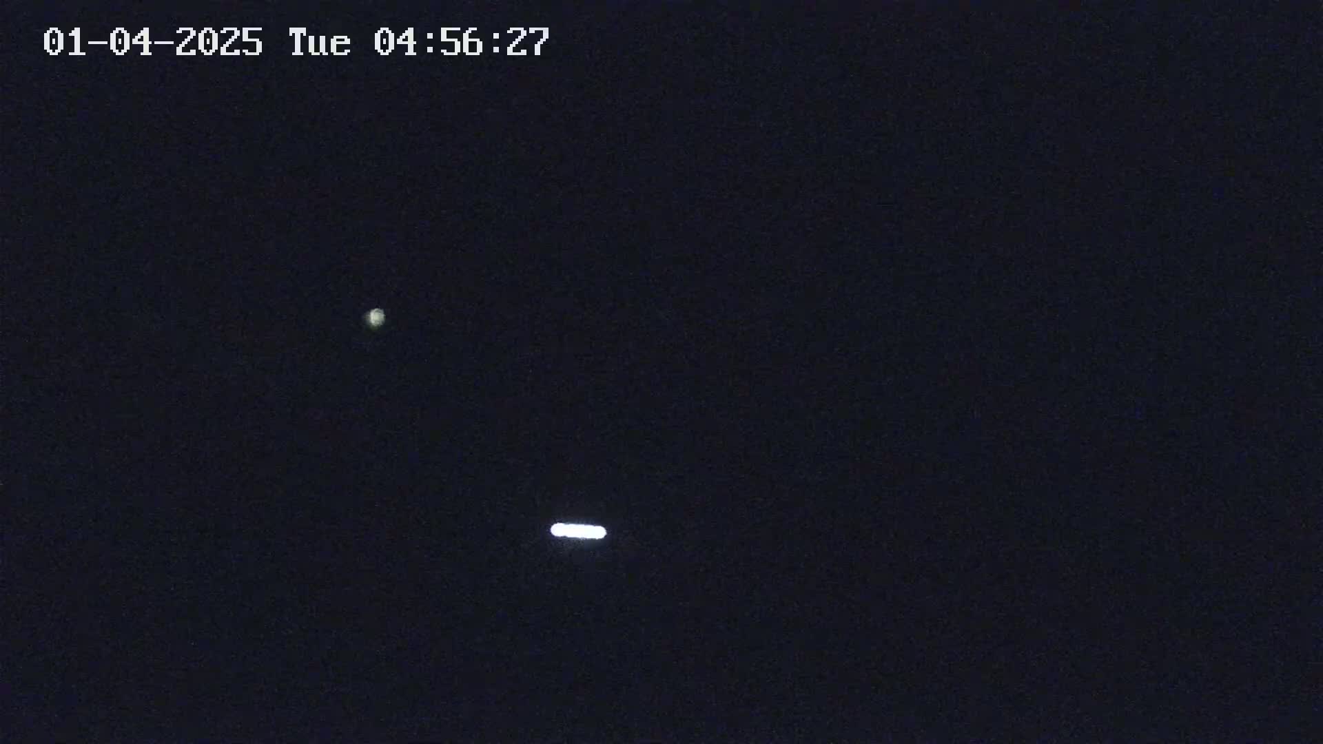 A dark night sky shows a bright point of light and a horizontal streak of light.