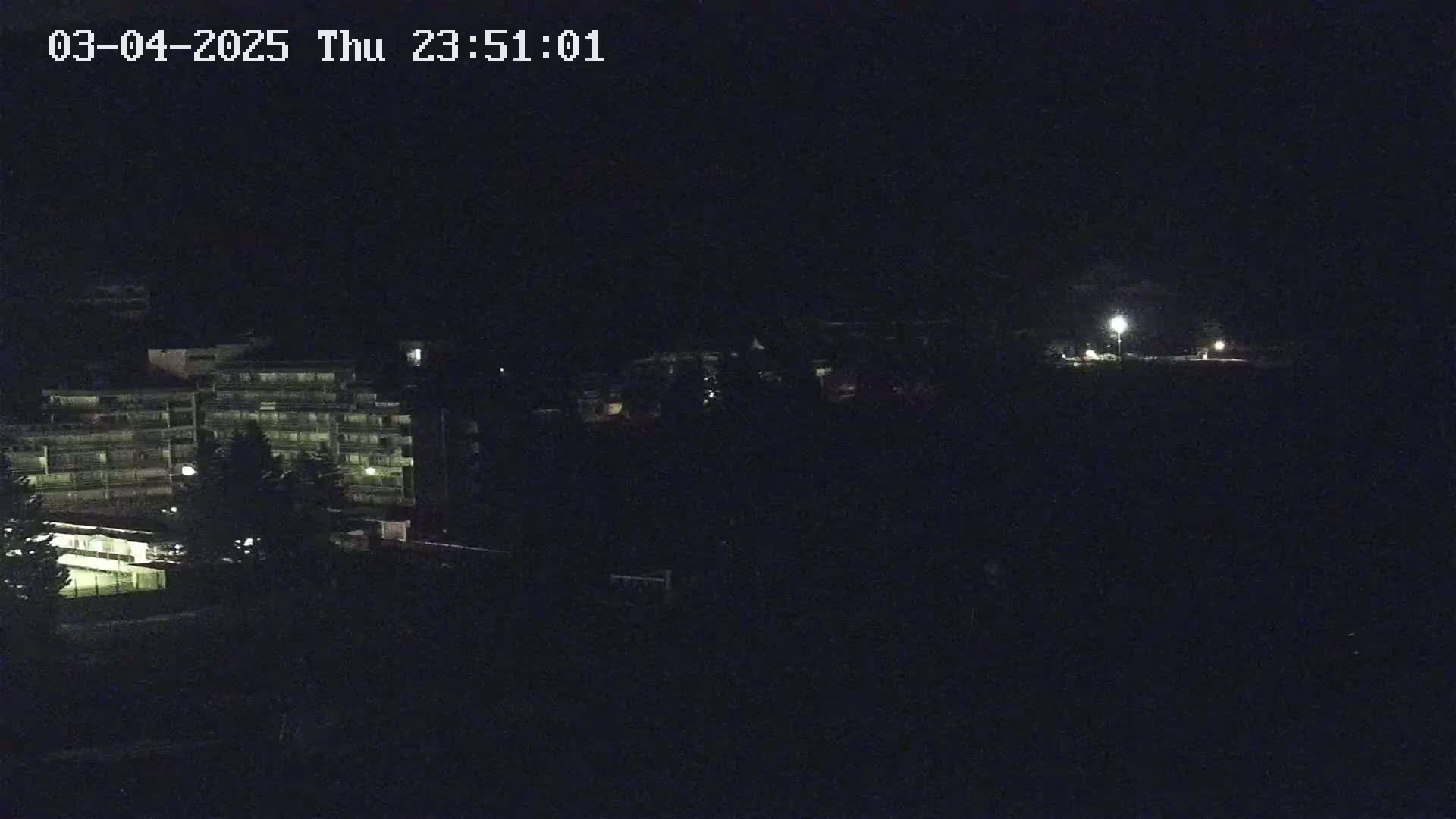 A multi-story building with illuminated windows is visible at night, along with some trees and dimly lit areas in the distance.