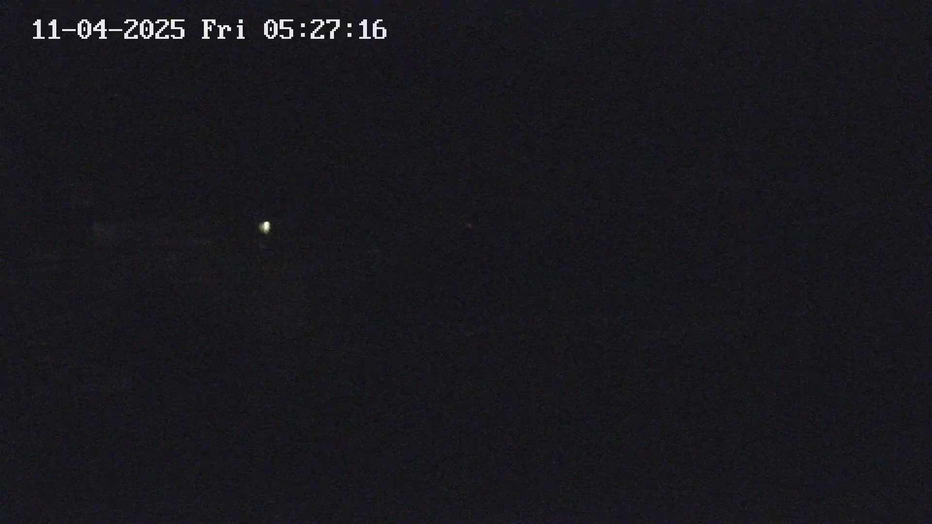 A dimly lit, dark scene at night shows a single faint light source in the distance.