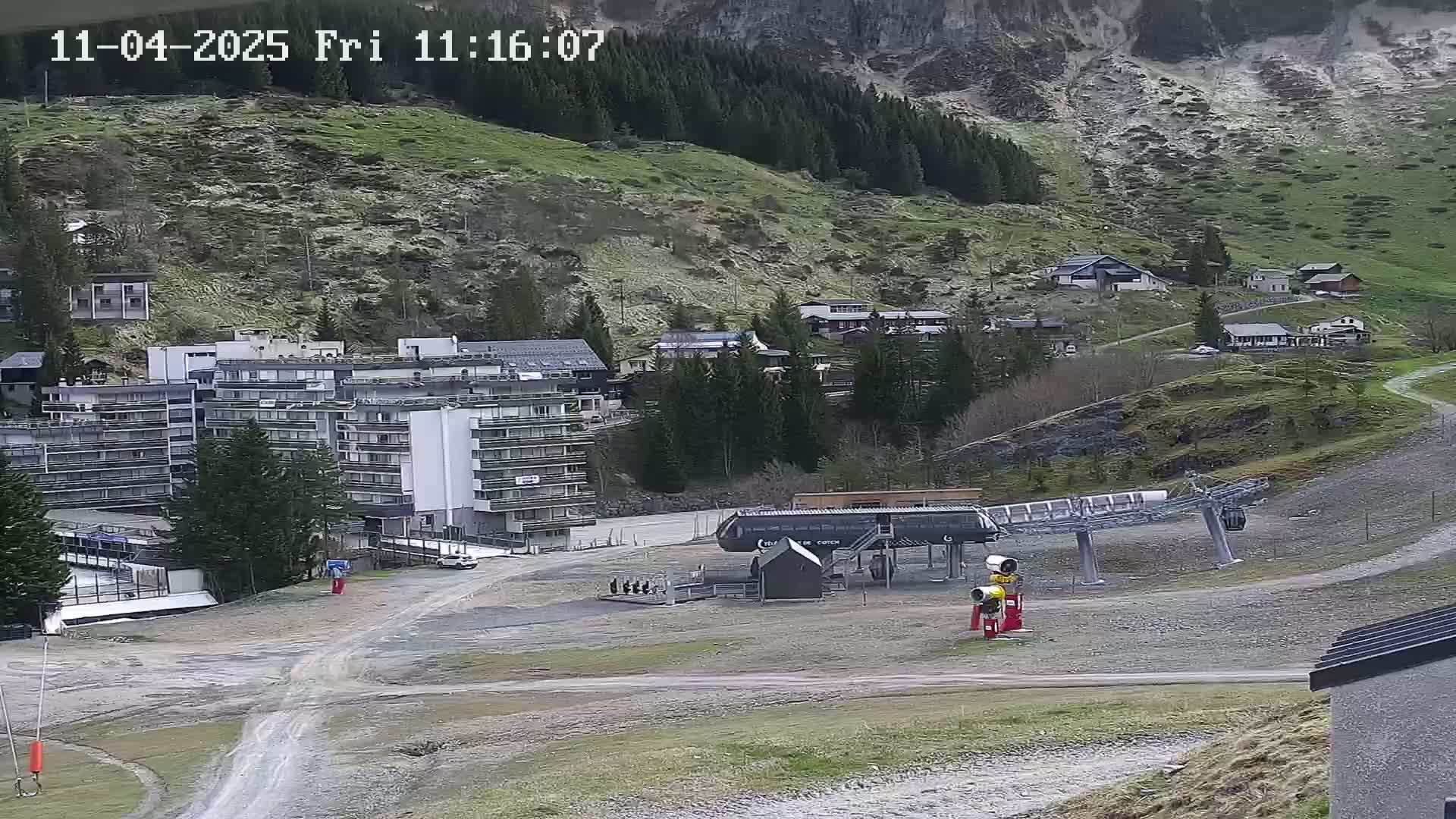 A mountainside village with buildings, a chairlift, and a gravel road is visible under overcast skies.