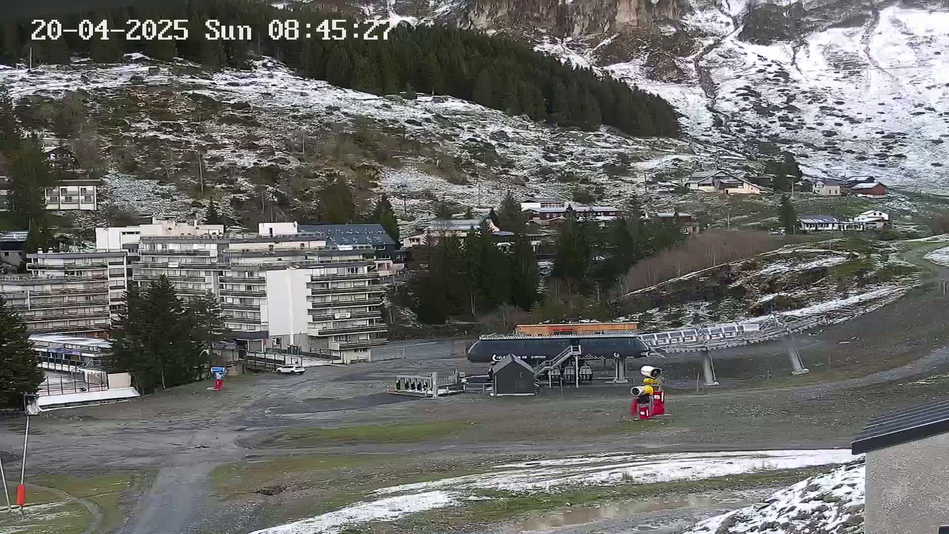 A ski resort with a chairlift and several buildings is partially covered in snow under overcast skies.