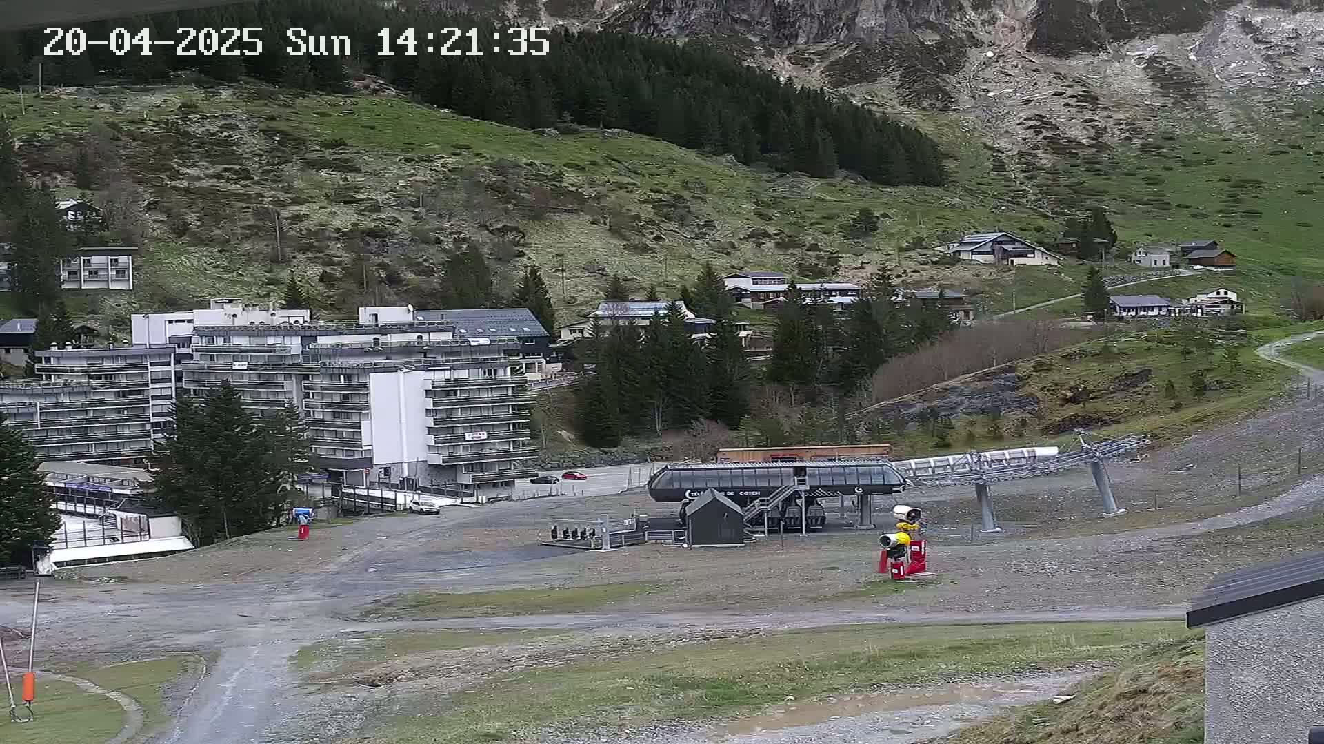 A ski resort with a chairlift, several buildings, and a large empty parking lot sits on a mountainside under a mostly cloudy sky.