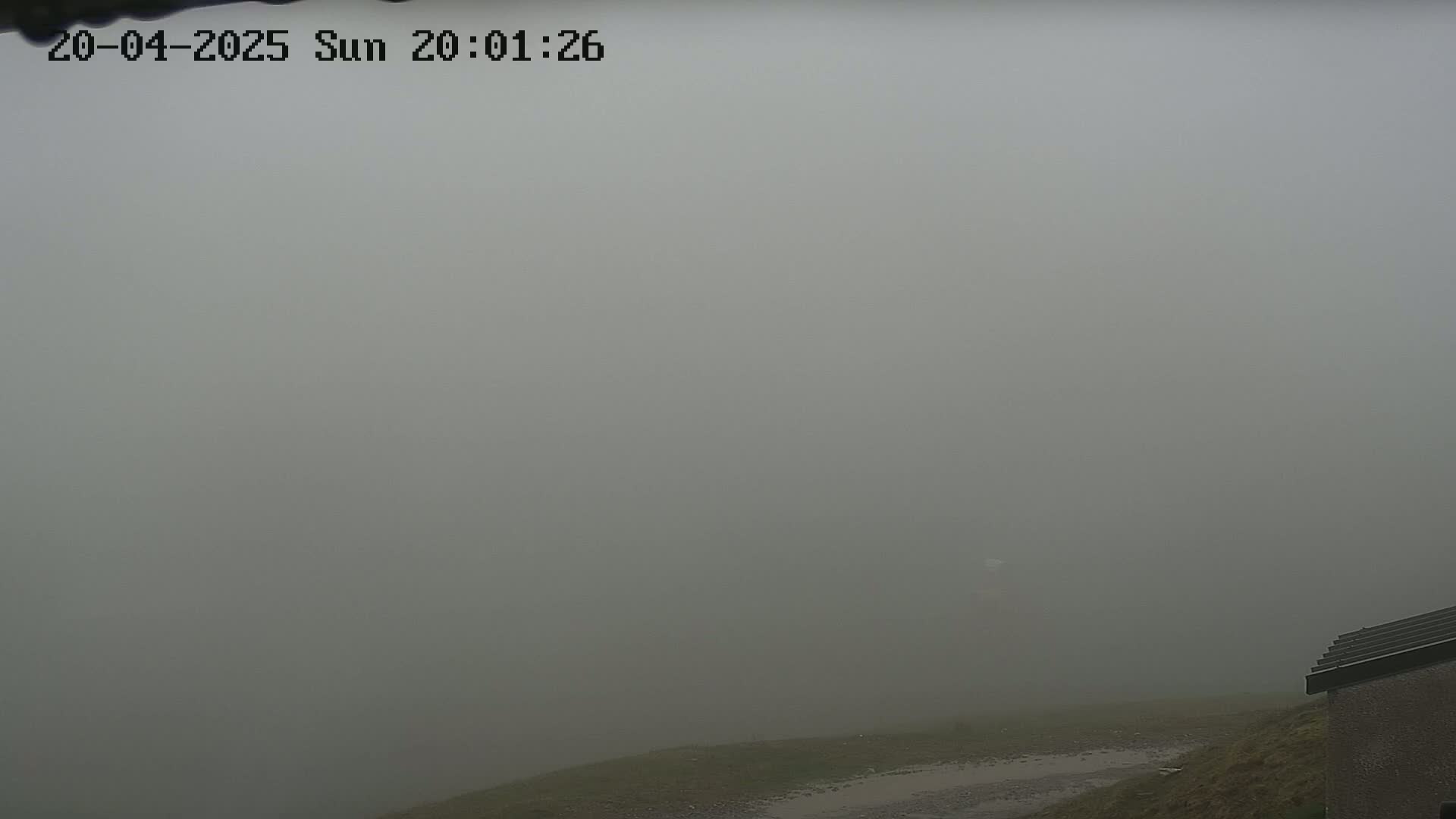 A very foggy outdoor scene shows a small portion of a building in the bottom right corner, with a muddy area and a hazy, indistinct background.