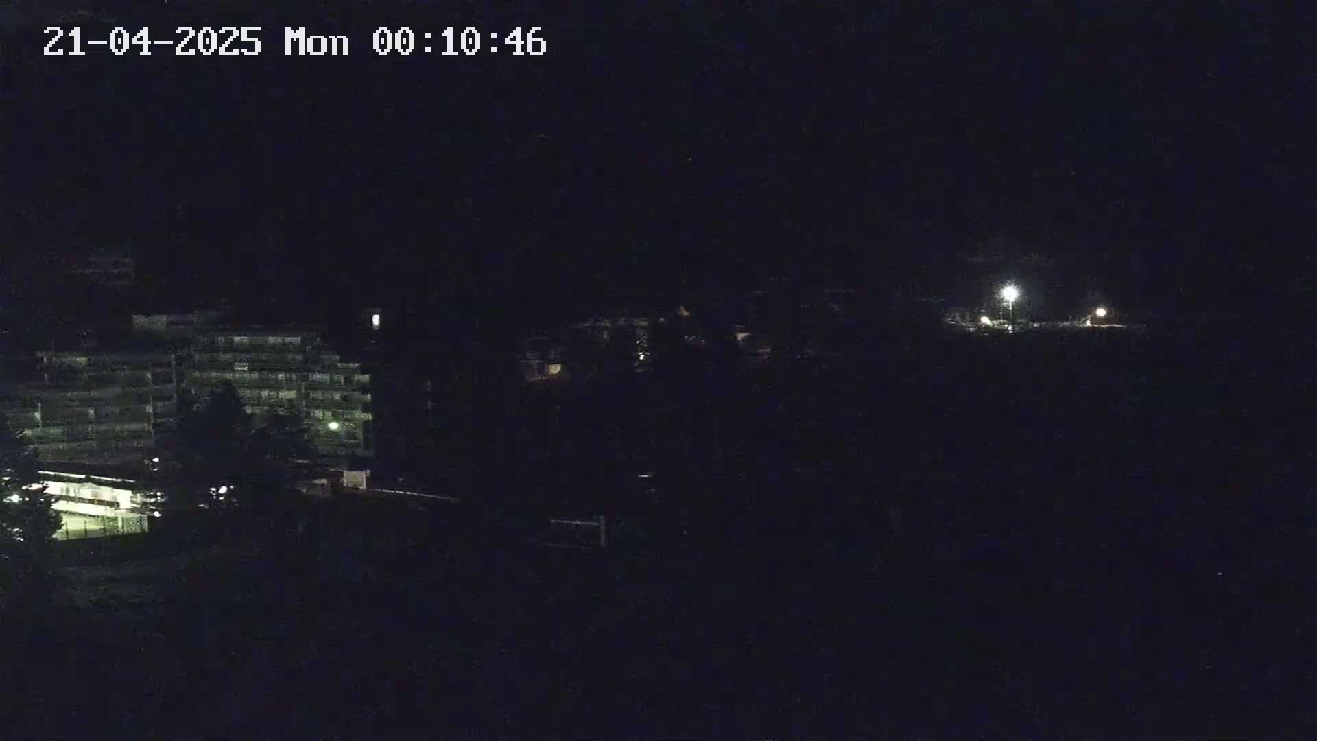 A dark nighttime scene shows a multi-story building with some surrounding trees and a few distant lights.
