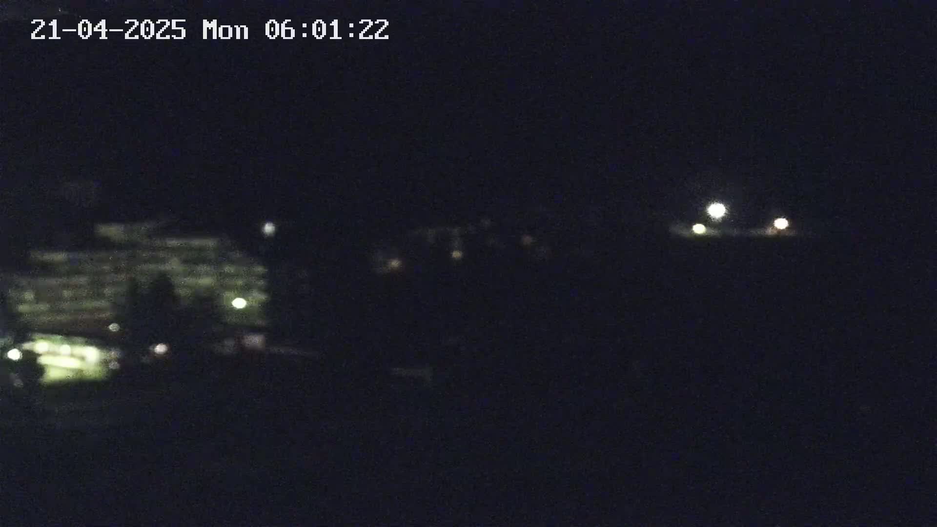 A blurry nighttime image shows a dimly lit building and a few distant lights under a dark sky.