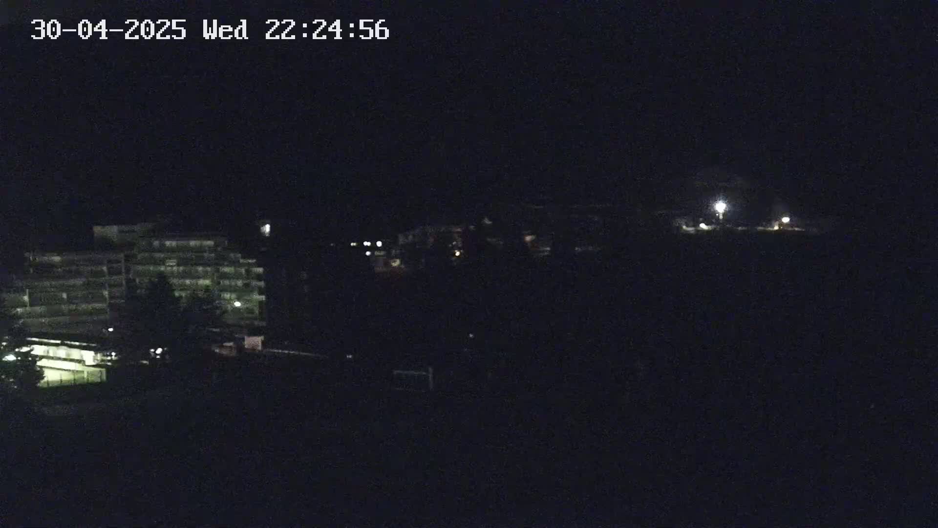 A dark nighttime scene shows a multi-story building and some sparsely lit areas in the distance.