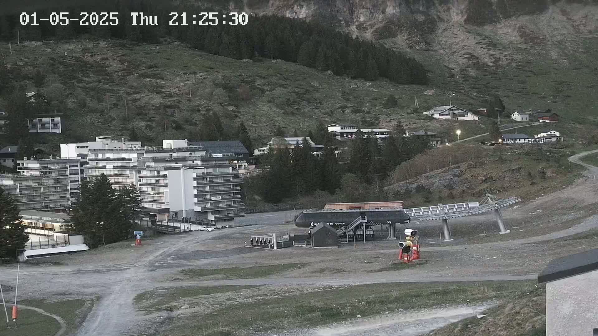 A large apartment building and chairlift are situated in a mountain valley at dusk, with sparsely vegetated hillsides in the background.