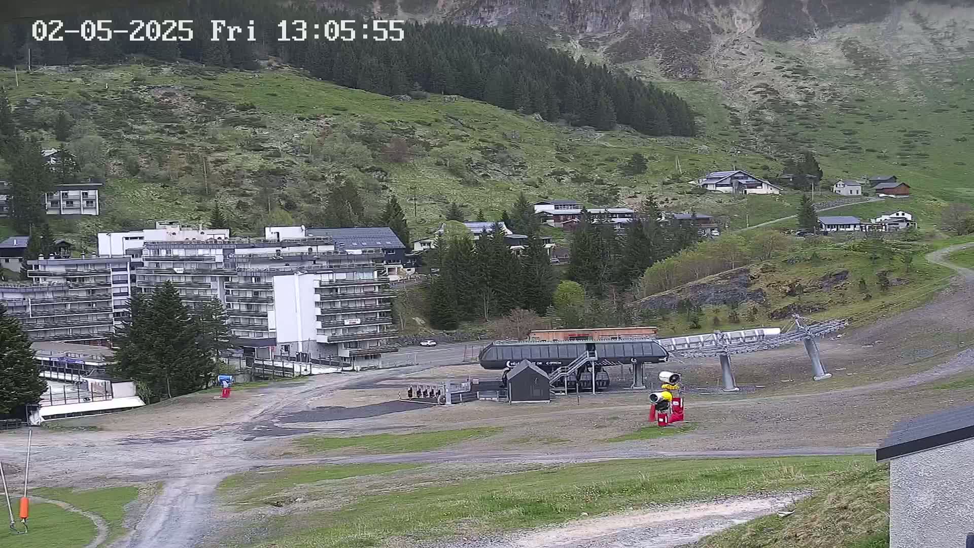 A ski lift base area with a large multi-story building, smaller buildings, and a mountainside with overcast skies.