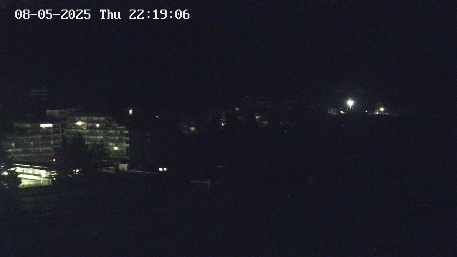 A dark nighttime scene shows a multi-story building with some lights on, and a few other faint lights in the distance.