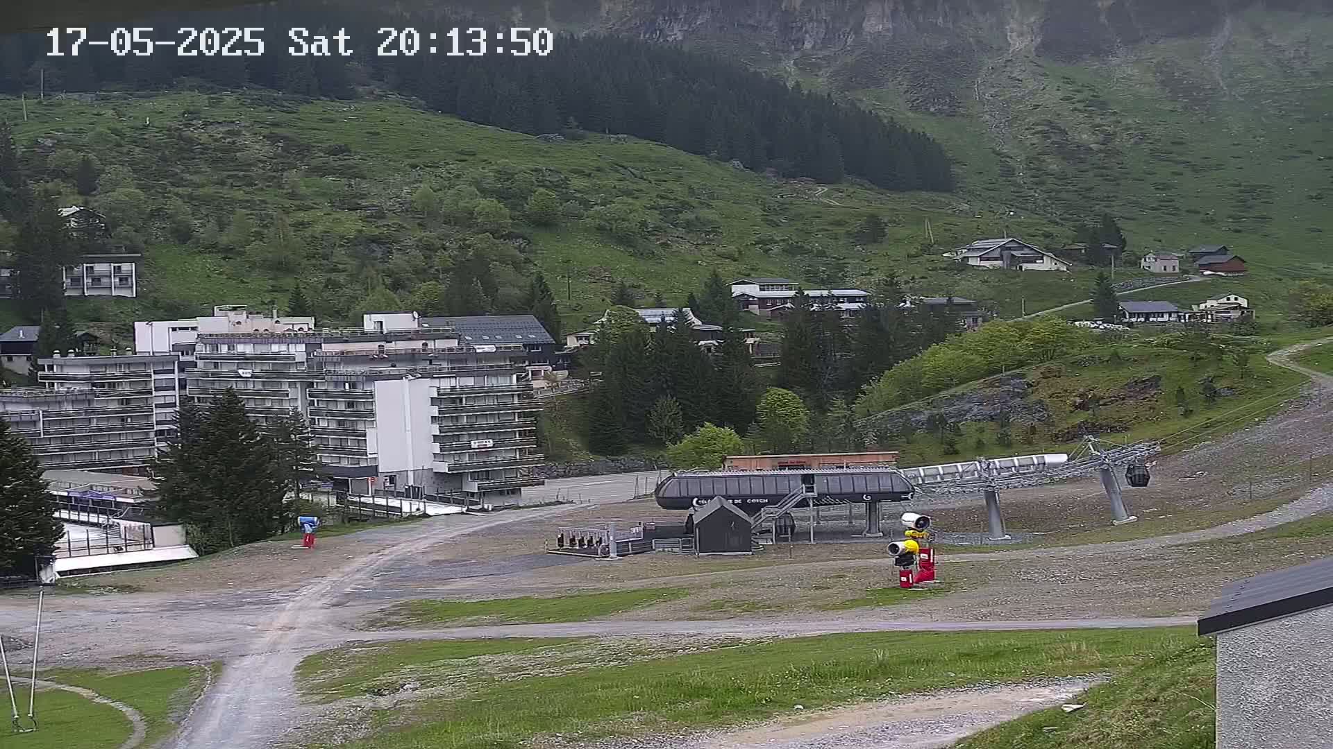 A mountainside village with several buildings, a chairlift, and a large apartment complex is seen on an overcast day.