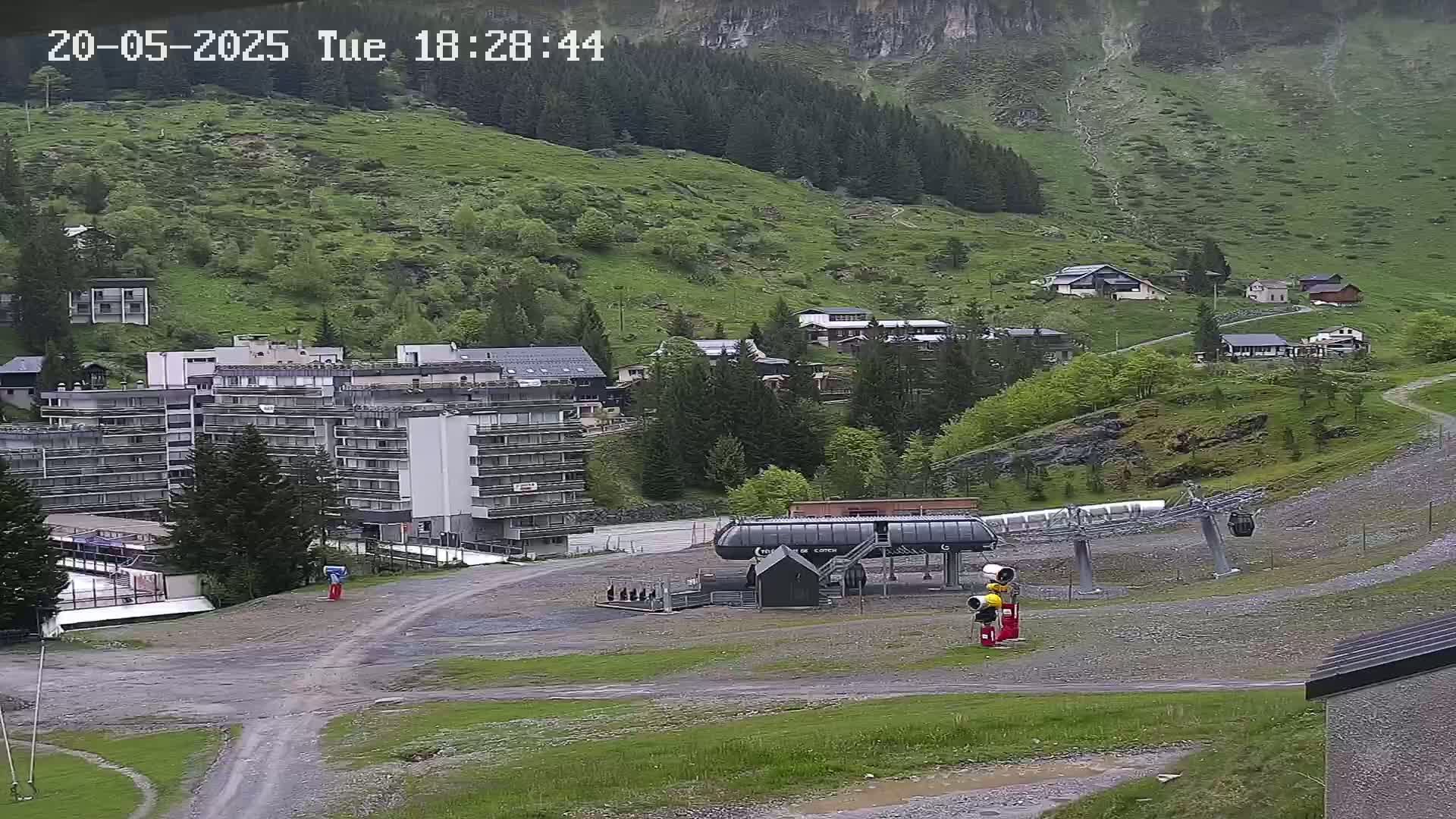 A chairlift and several buildings are situated on a grassy hillside, with overcast weather conditions.