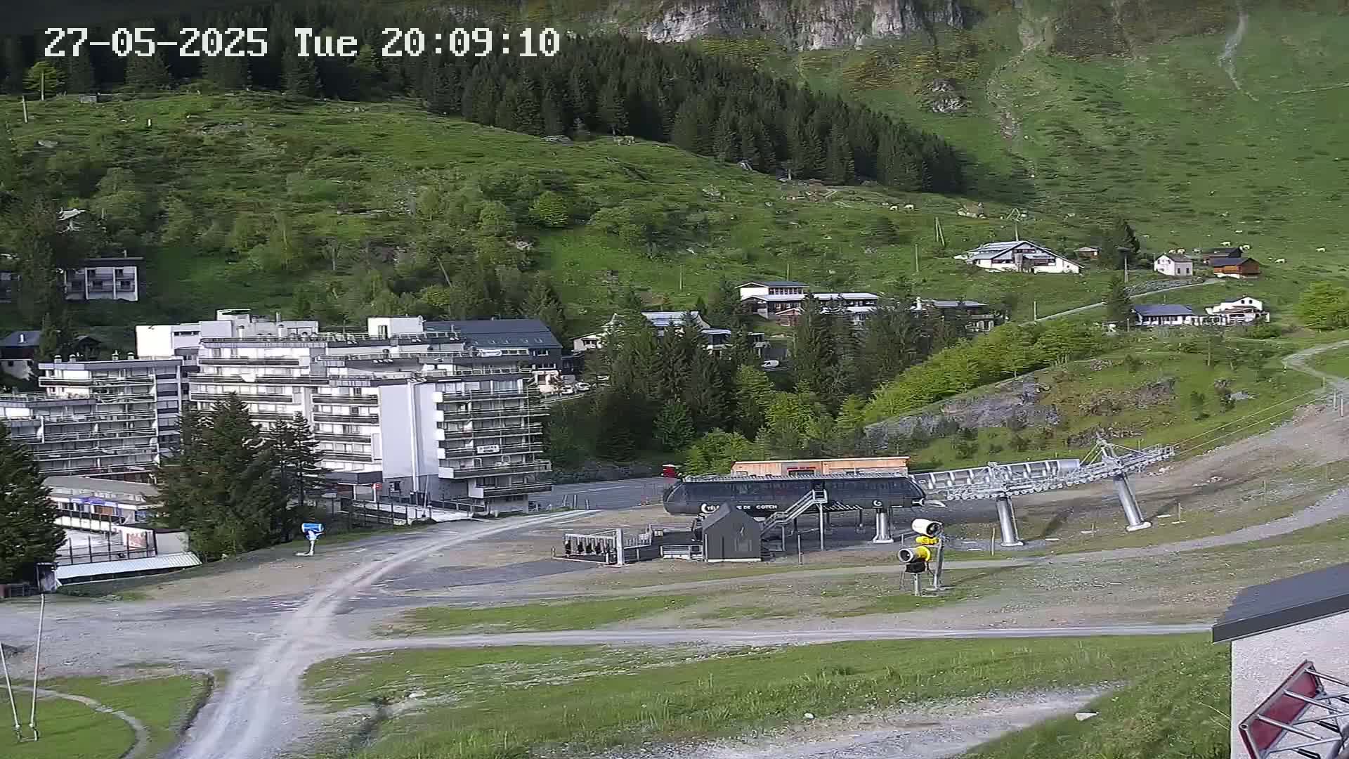 A mountainside village with a large apartment building and a chairlift, under a clear sky.
