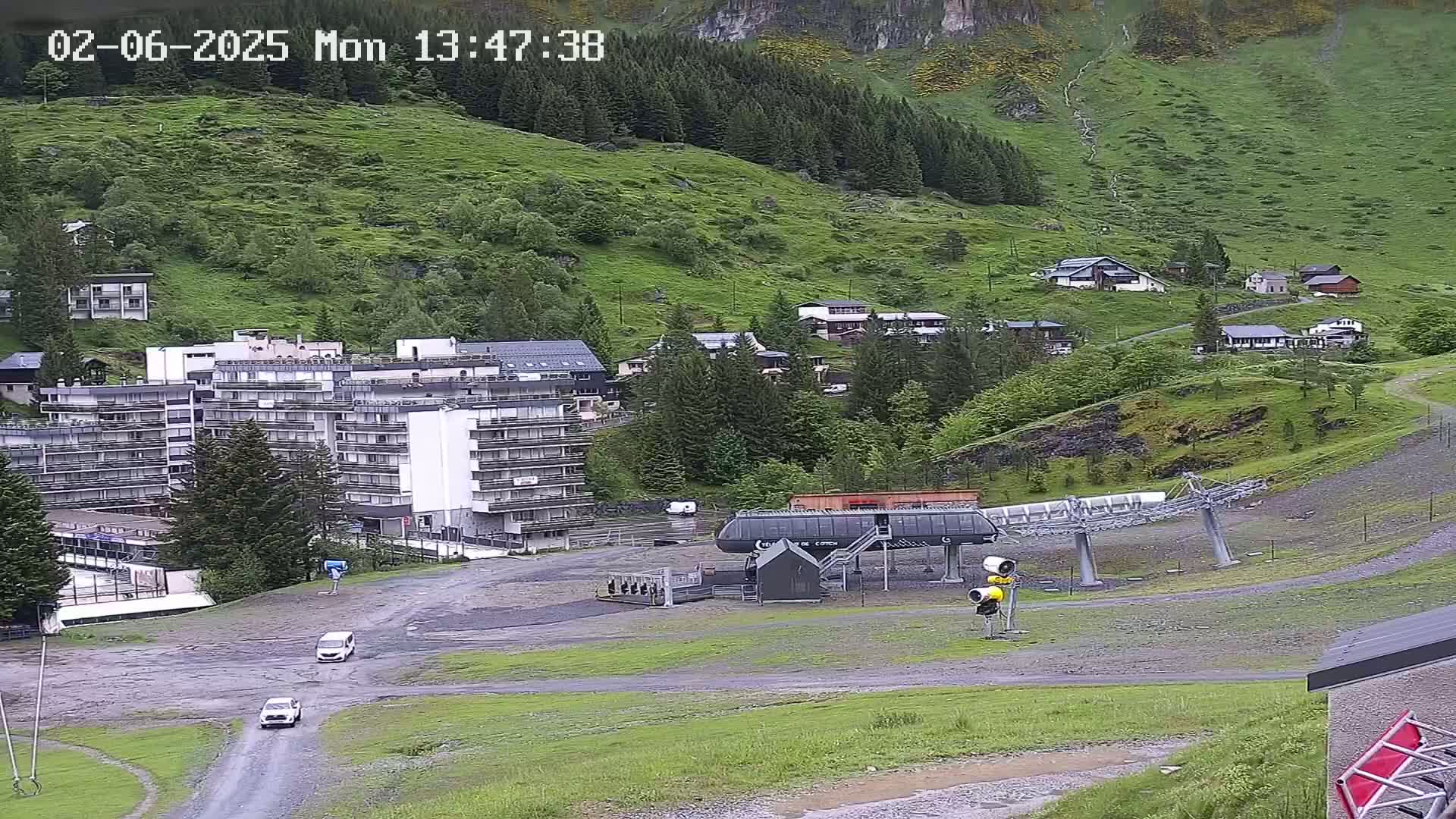 A mountainside village with several buildings, including a large apartment complex and a chairlift, is visible under an overcast sky.