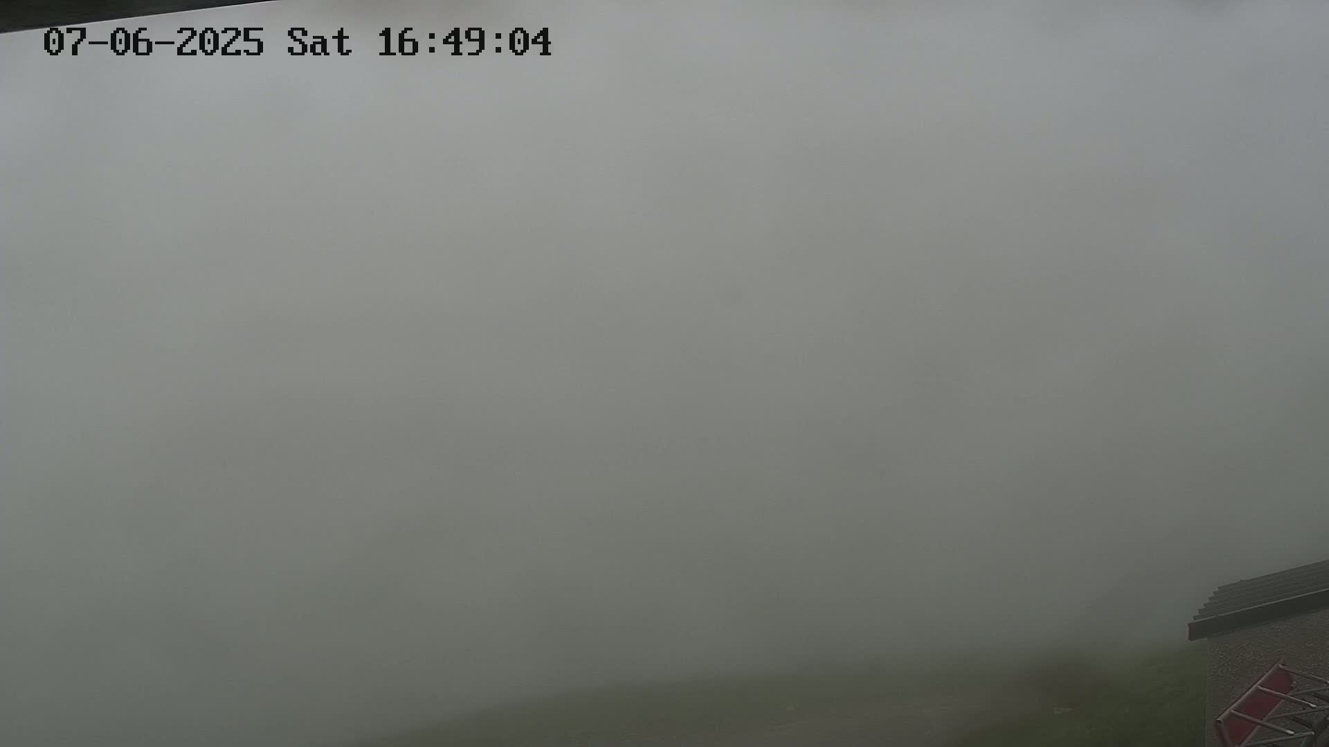 A thick fog obscures the view of a landscape, with only a portion of a building visible in the bottom right corner.