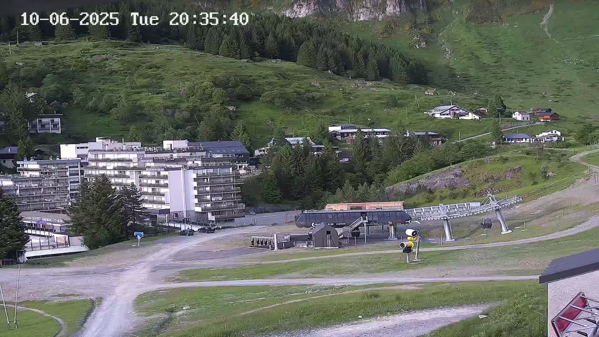 A mountainside village with a large apartment building, a chairlift, and several smaller houses is visible under twilight conditions.