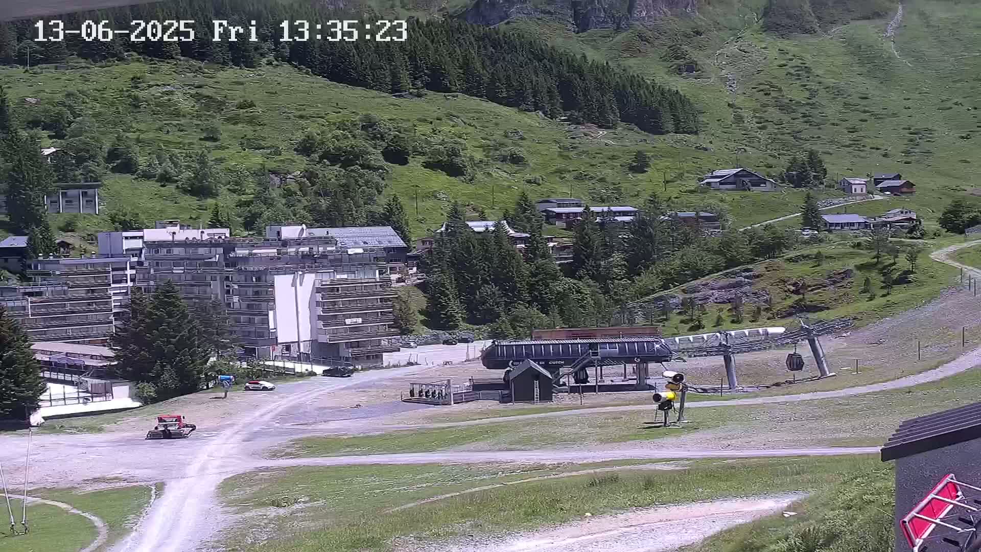 A mountainside village with a large apartment building, a ski lift, and several smaller buildings is visible on a sunny day.