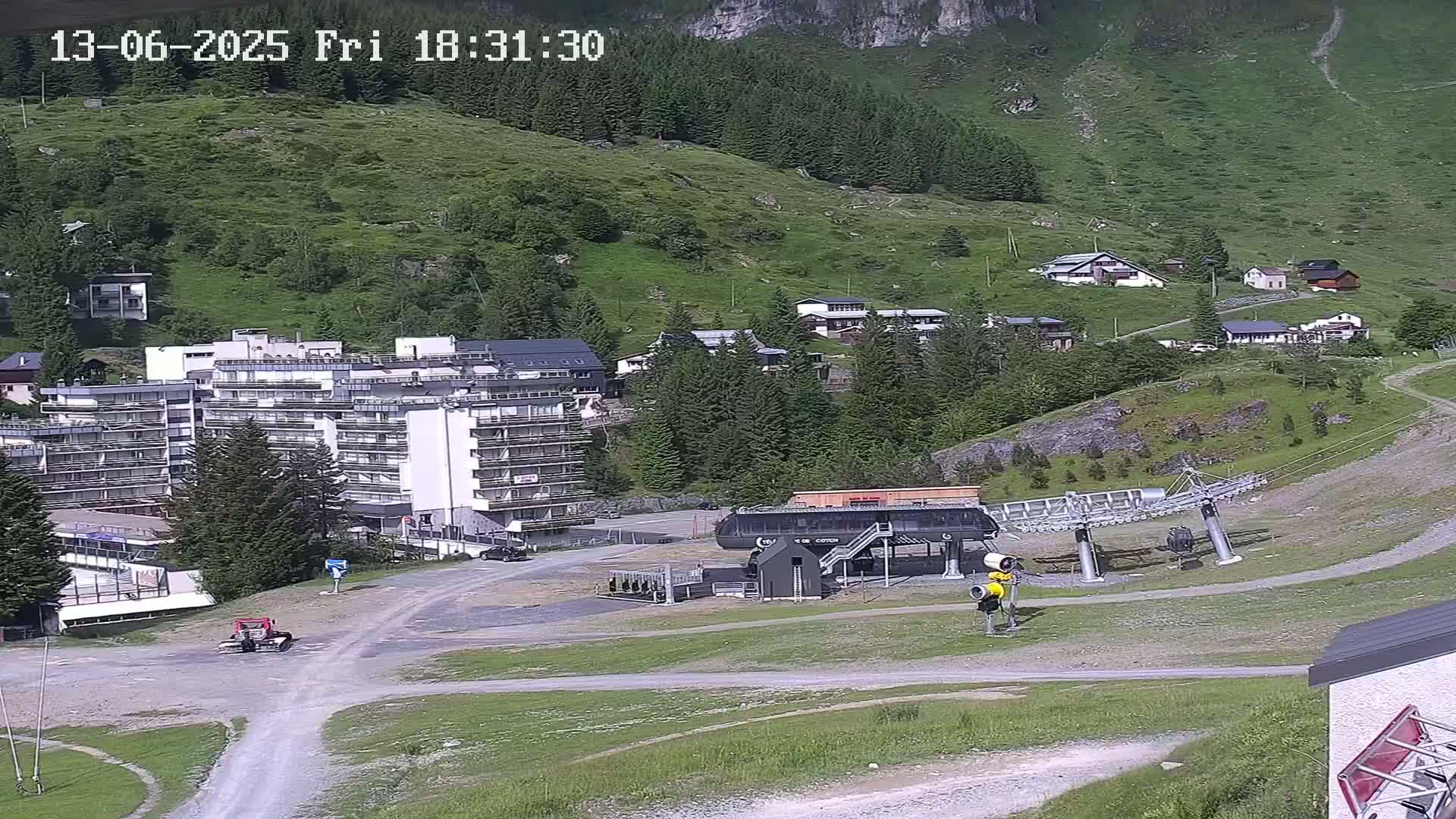A mountainside village with a large apartment building, a chairlift, and several smaller buildings, all under sunny skies.