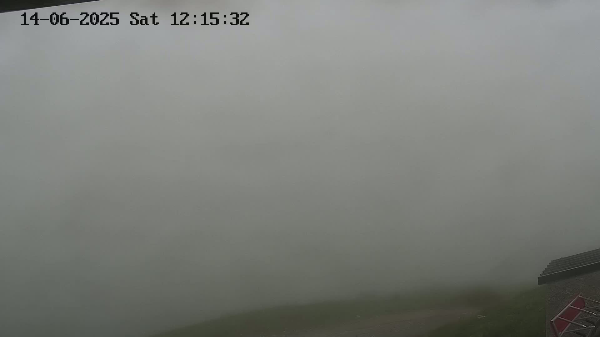 A foggy outdoor scene shows a small portion of a building and ground, mostly obscured by dense fog.