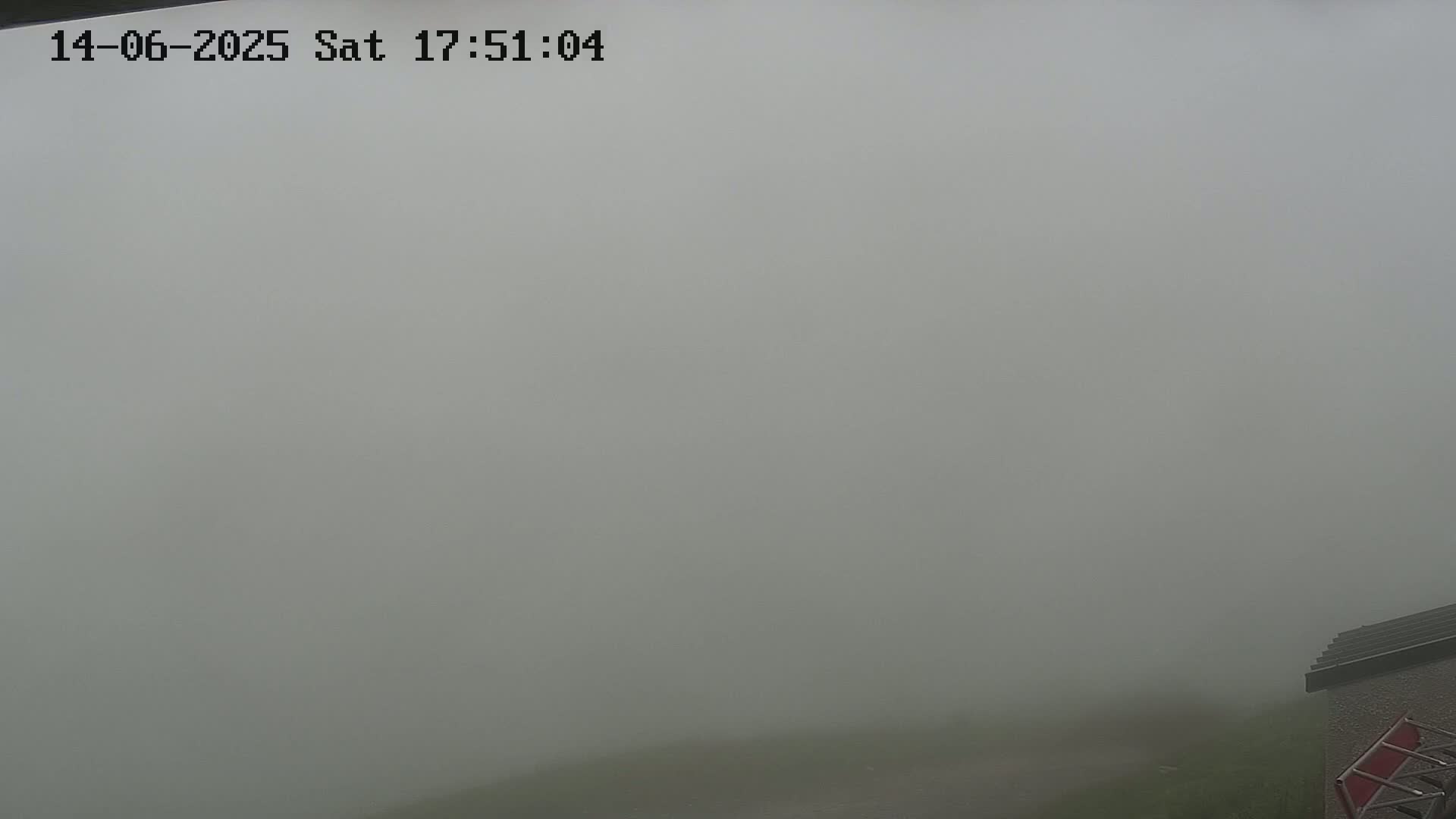 A thick fog obscures the view of a mostly unseen landscape, with only a small portion of a building visible in the bottom right corner.